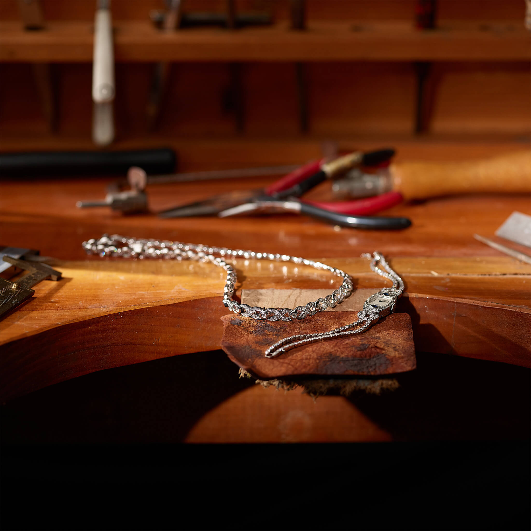 Handcrafted bespoke white gold necklace and an old heirloom watch resting on a jeweller's bench