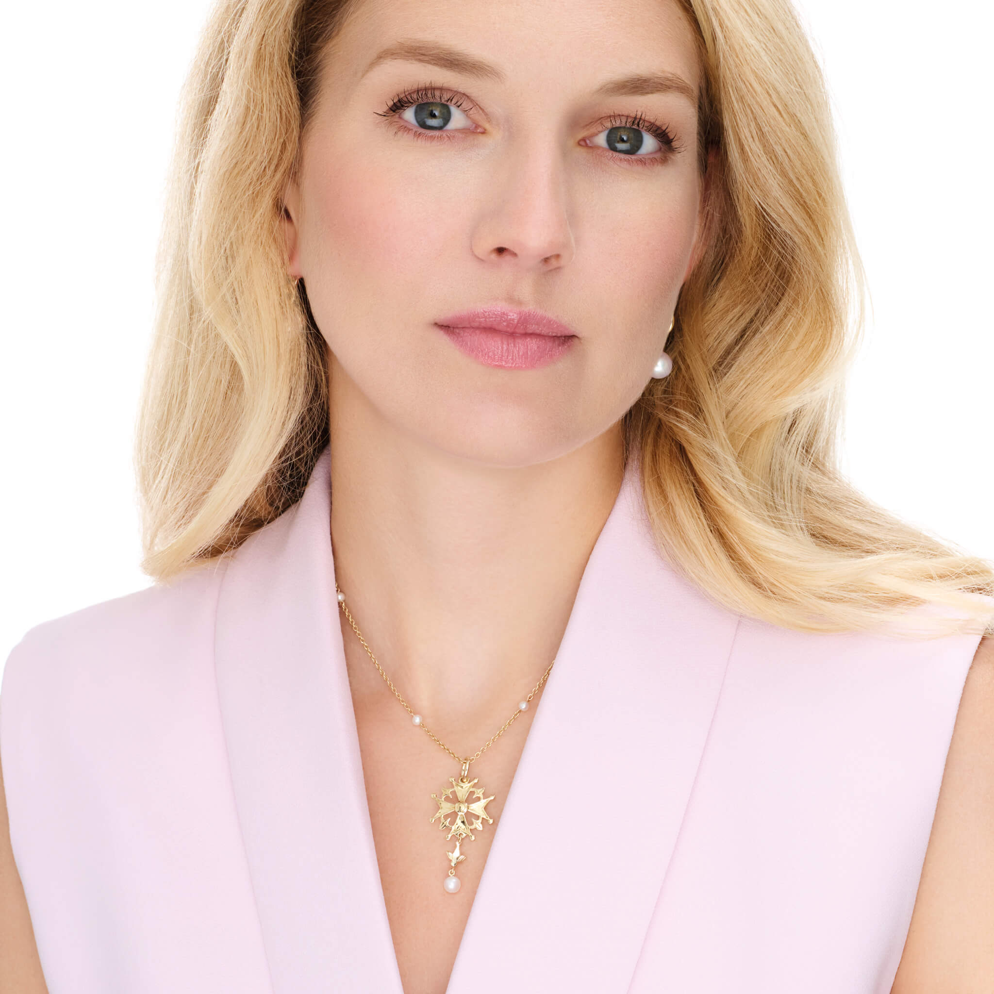 Model wearing a handcrafted precious metal Huguenot cross pendant with pearl, birthstone of June.