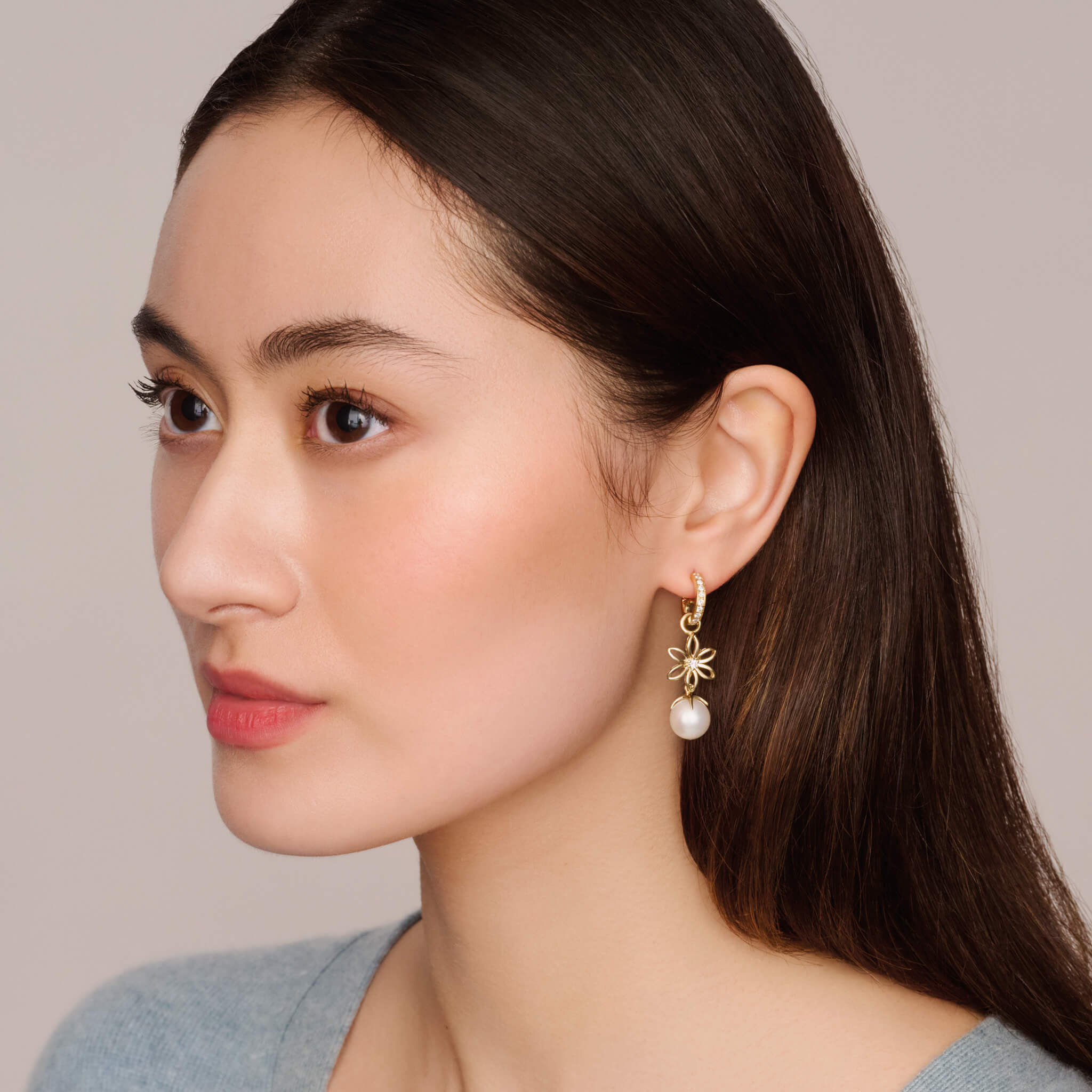 model wears handcrafted yellow gold flower-shaped earrings drops designs set with diamonds, birthstone of April, hanging from hoop earrings.