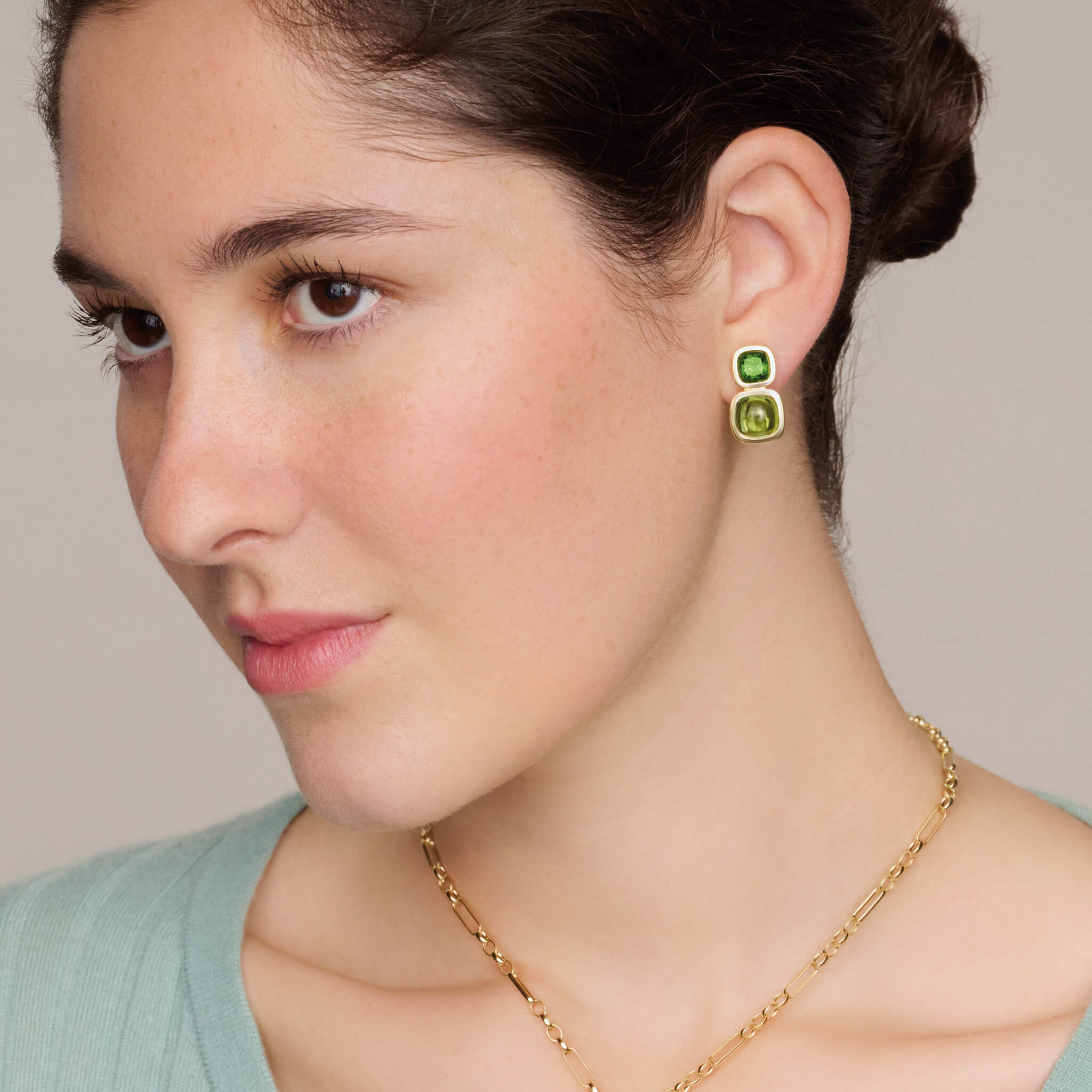 model wears handcrafted 18ct yellow gold square shaped earrings featuring green tourmaline and cabochon peridot gemstones.