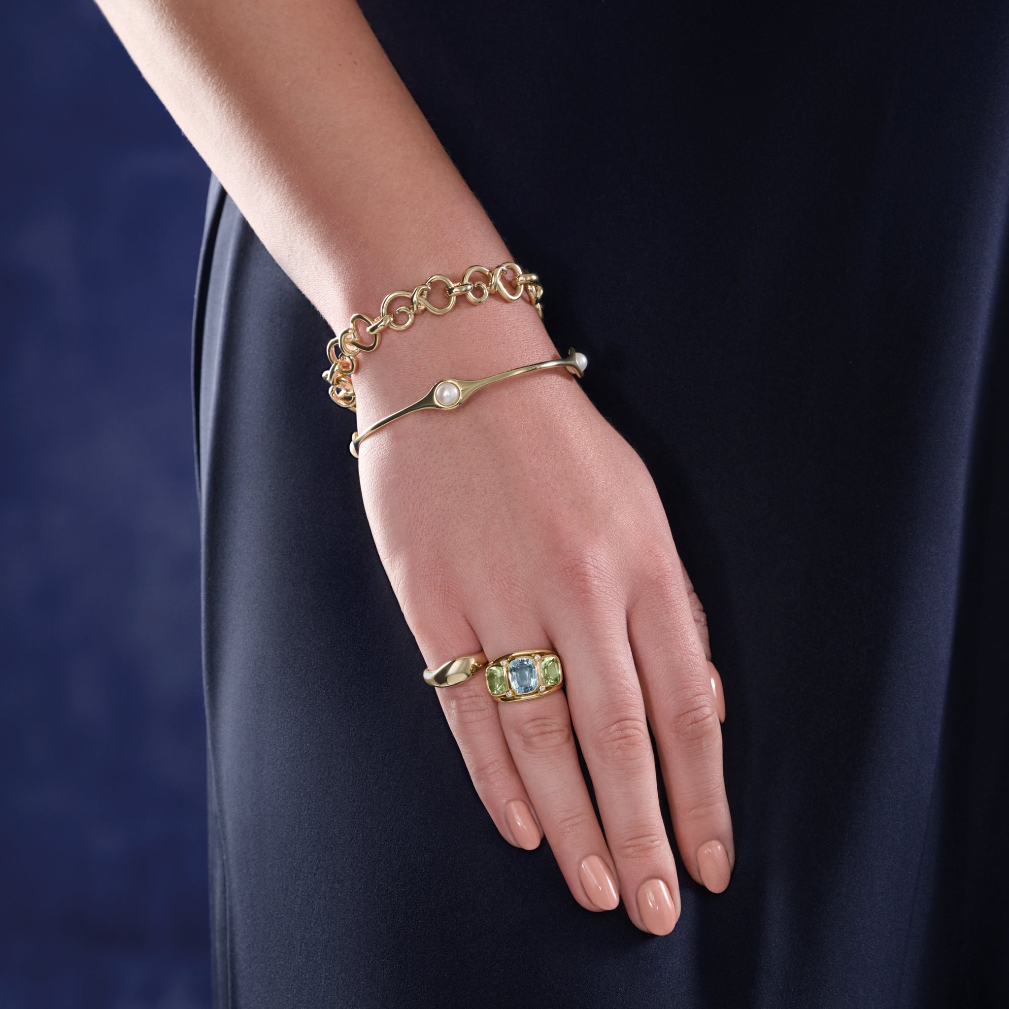 Model wearing a handcrafted 18ct yellow gold ring featuring rectangular shaped precious gemstones and diamonds and a yellow gold bangle featuring four pearls.
