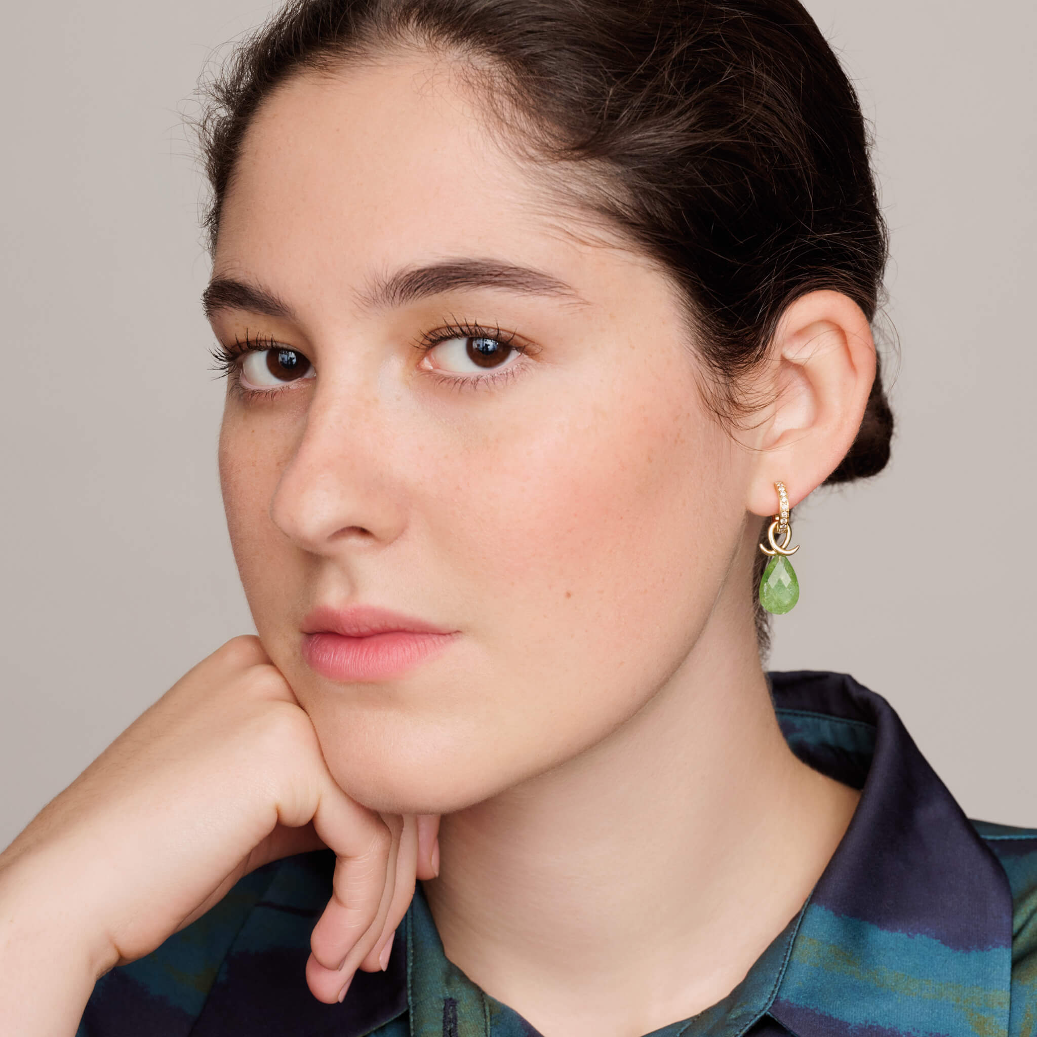 model wears handcrafted 9ct yellow gold earring drops with oval tsavorite garnet and an oval loop shape crossing over.