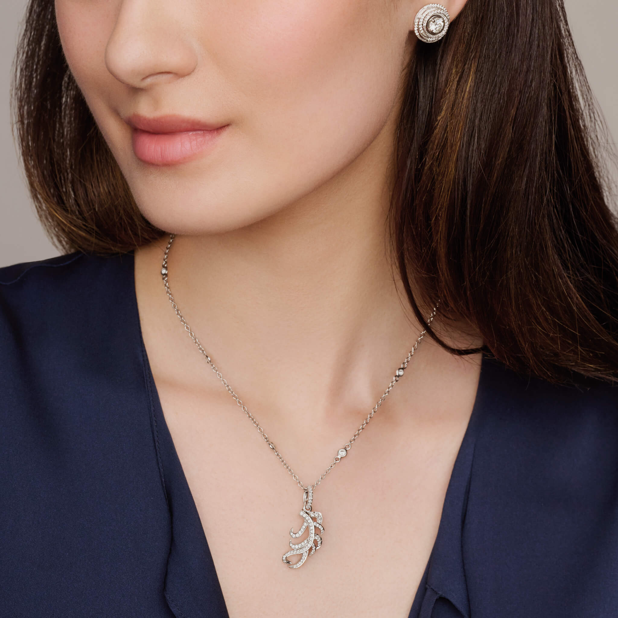 Model wears handcrafted necklace pendant in the shape of a feather plume in 18ct white gold with diamond pave