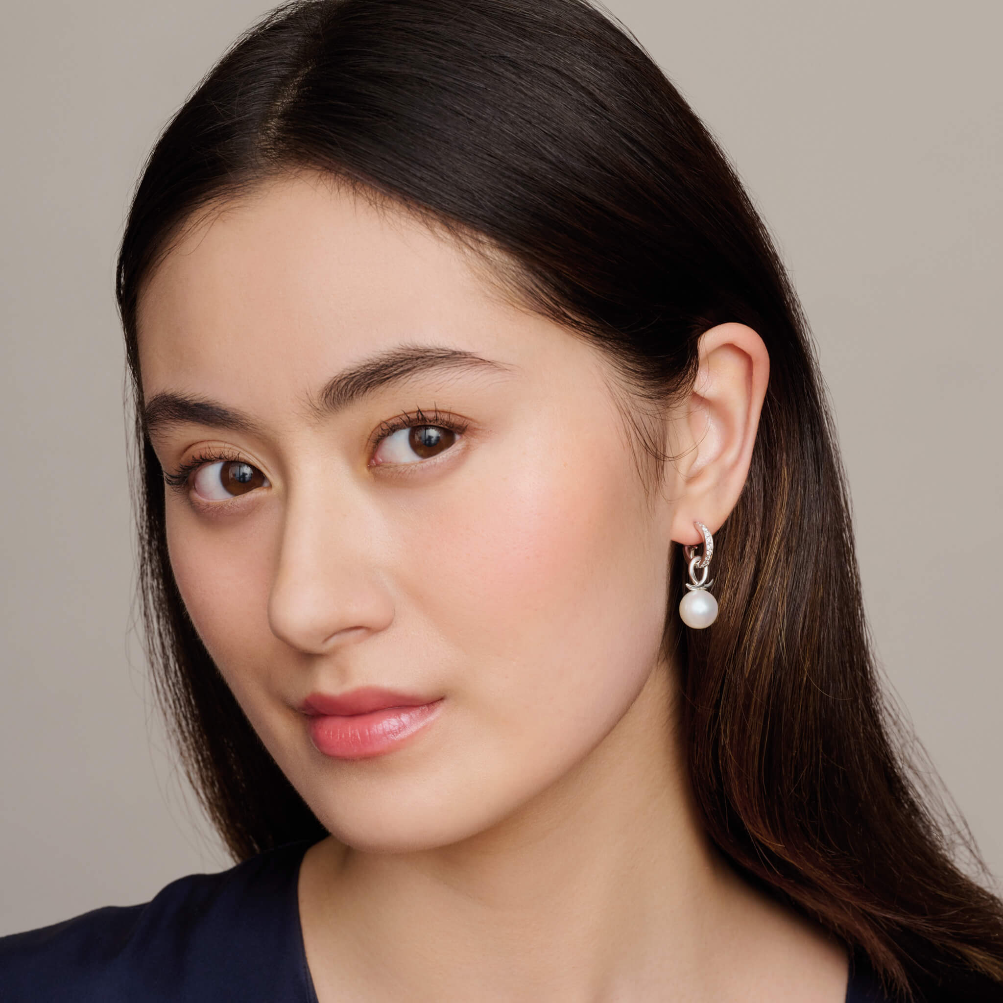 model wears handcrafted silver earring drops with round pearl and an oval loop shape crossing over.