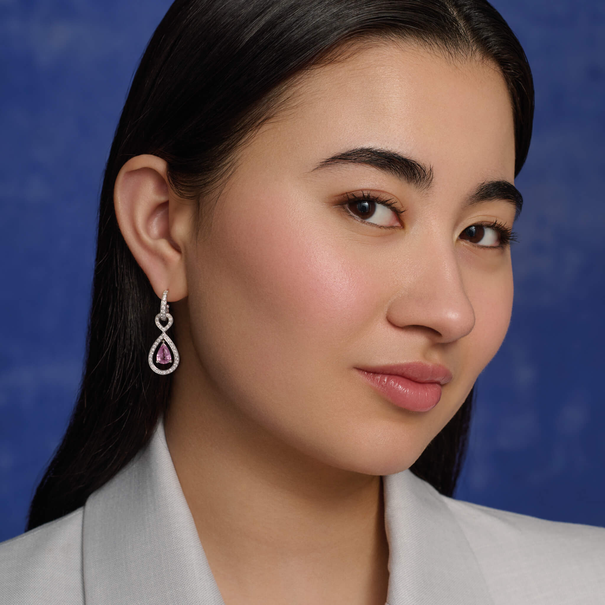model wears handcrafted 18ct white gold earring drops featuring a central pink sapphire surrounded by diamonds.
