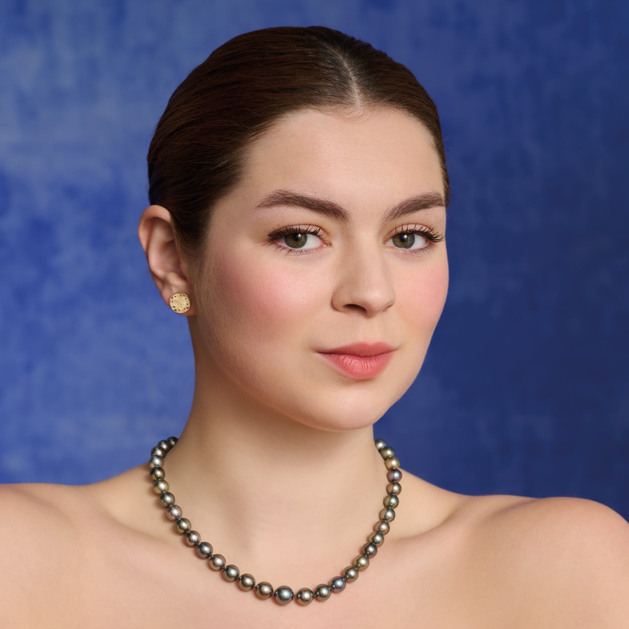 Model wears handcrafted 9ct yellow gold circular earring studs with a cross-like motif in the centre.