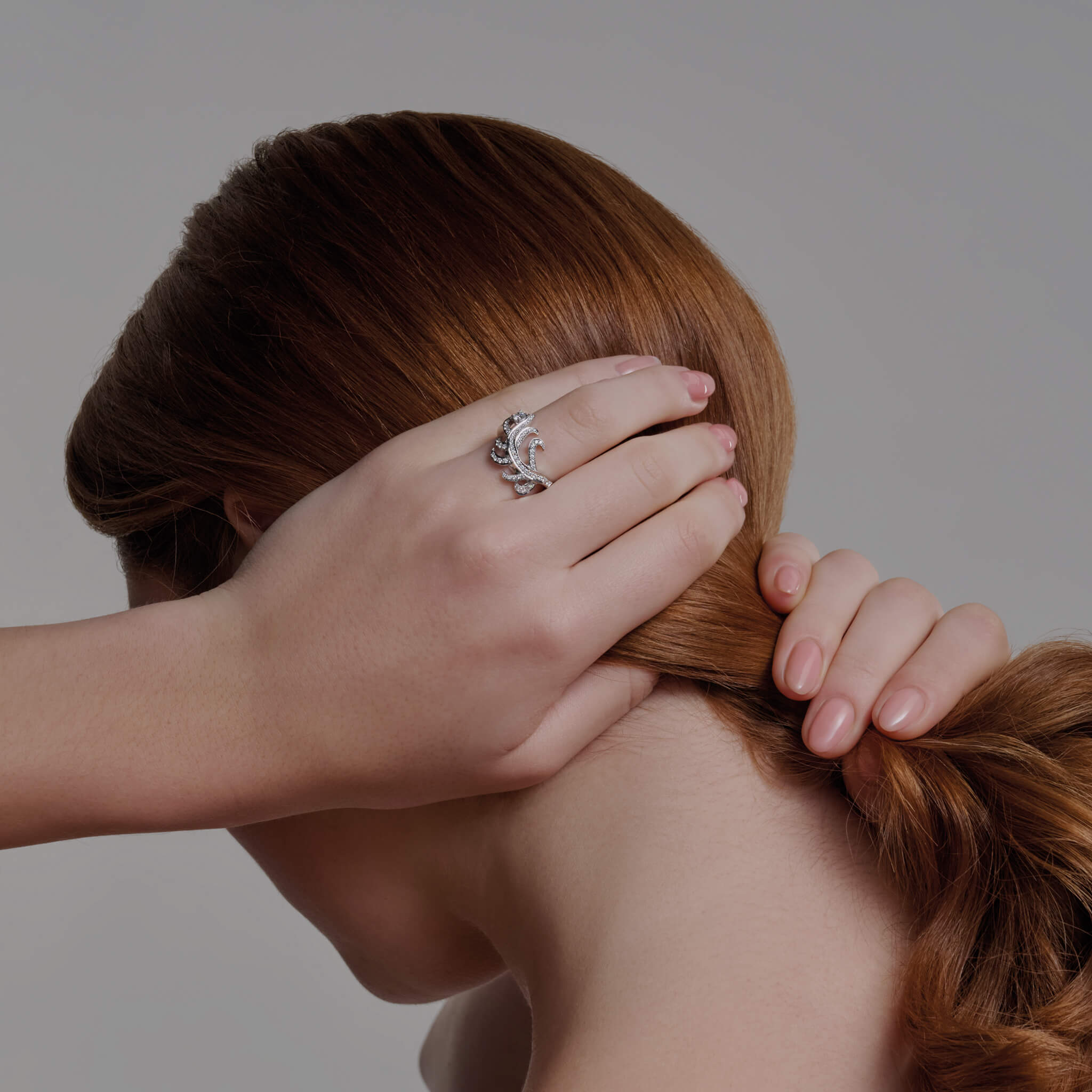 Model wears handcrafted ring in the shape of a feather plume in 18ct white gold with diamond pavé and a central round diamond. 