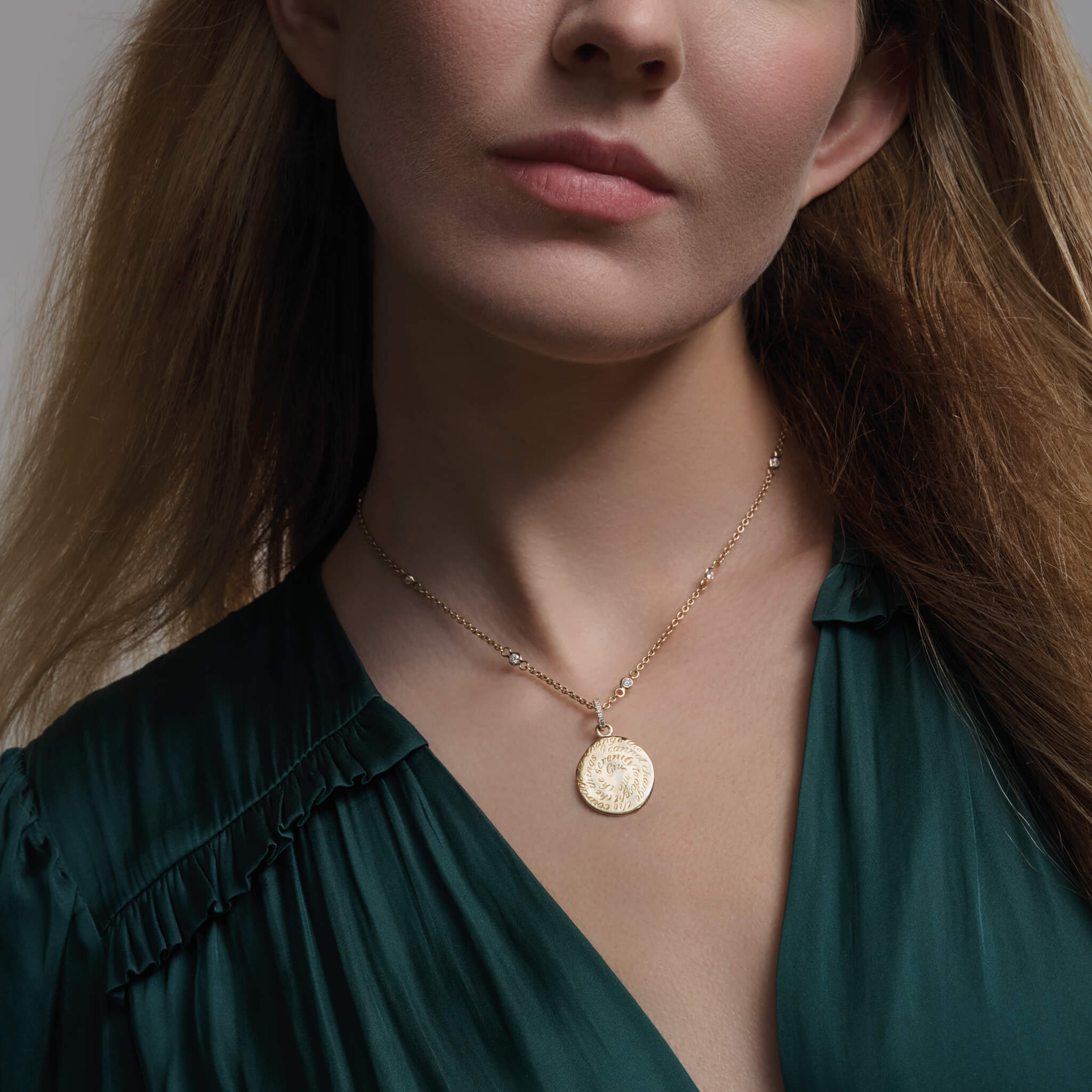 Model wearing a handcrafted round yellow gold pendant necklace with diamond pave engraved with a quote on discovery.