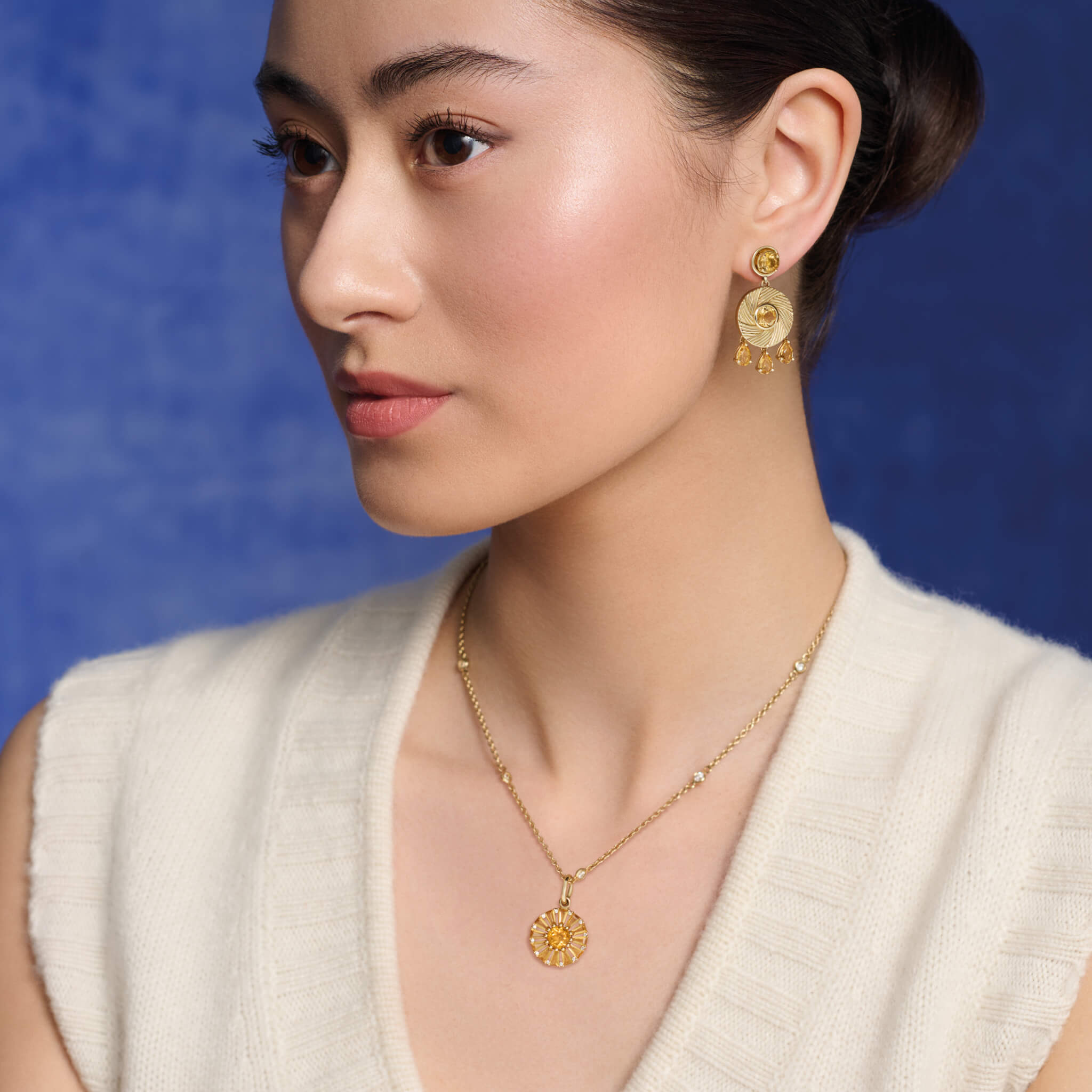 Model wears handcrafted yellow gold necklace pendant featuring a circular arrangement of colourful gemstones and  diamonds.