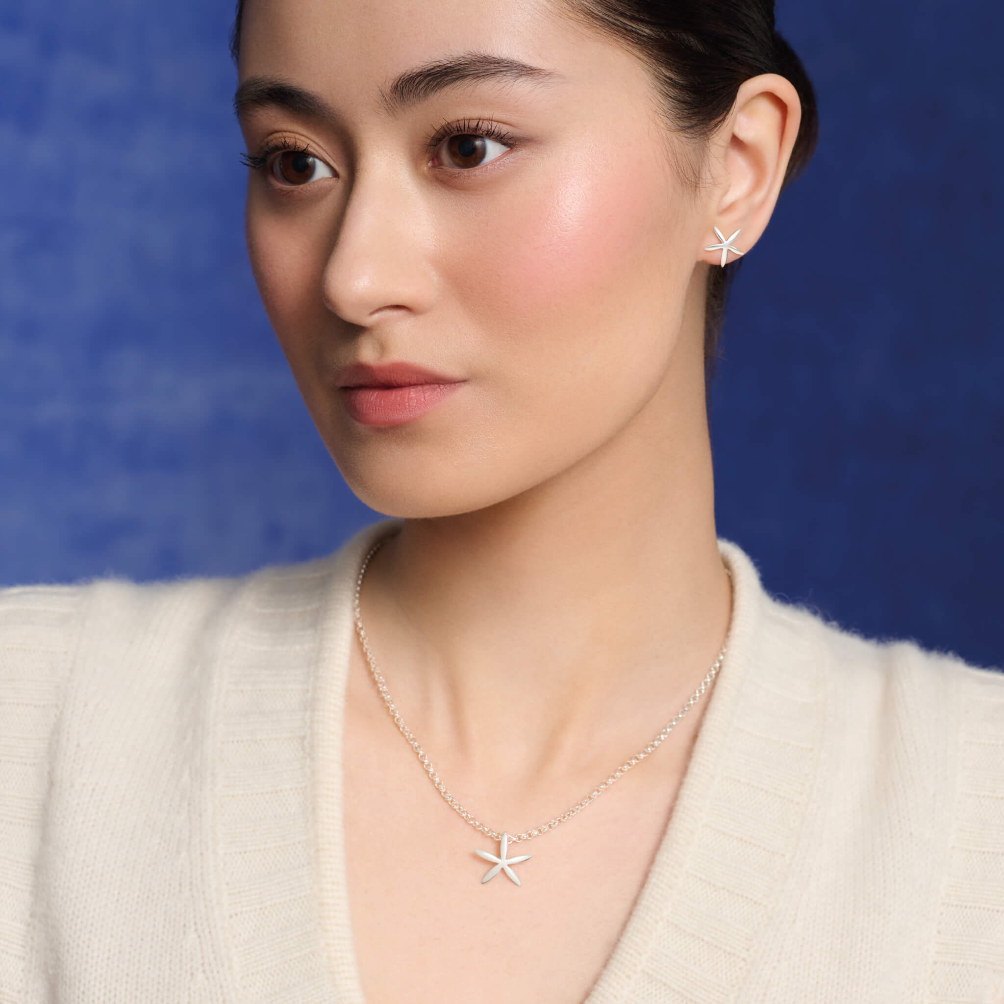 Model wears starfish shaped necklace pendant in precious metal.