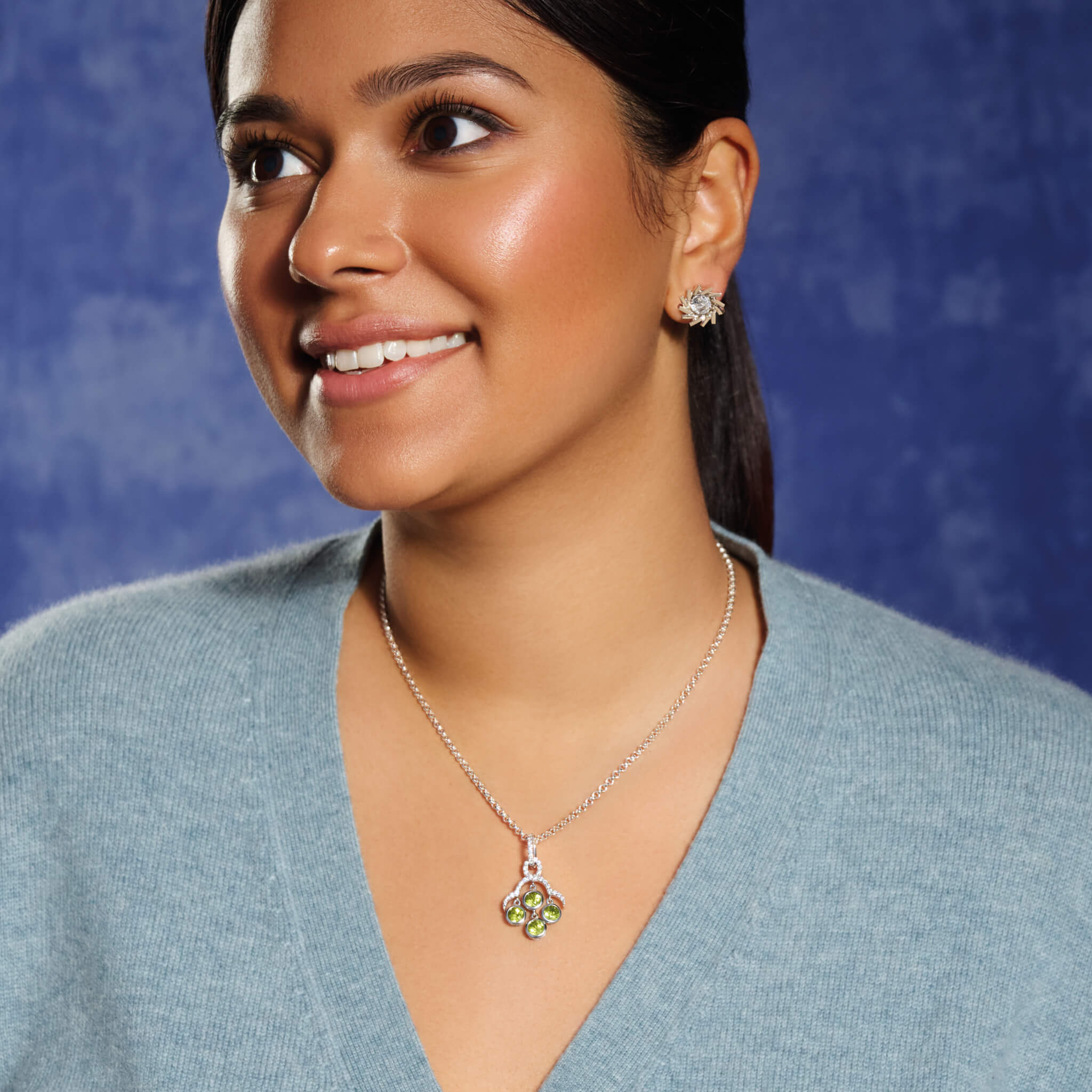 Model wears handcrafted white gold necklace pendant inspired by acai berries featuring four peridot gemstones and diamonds, on a chain.