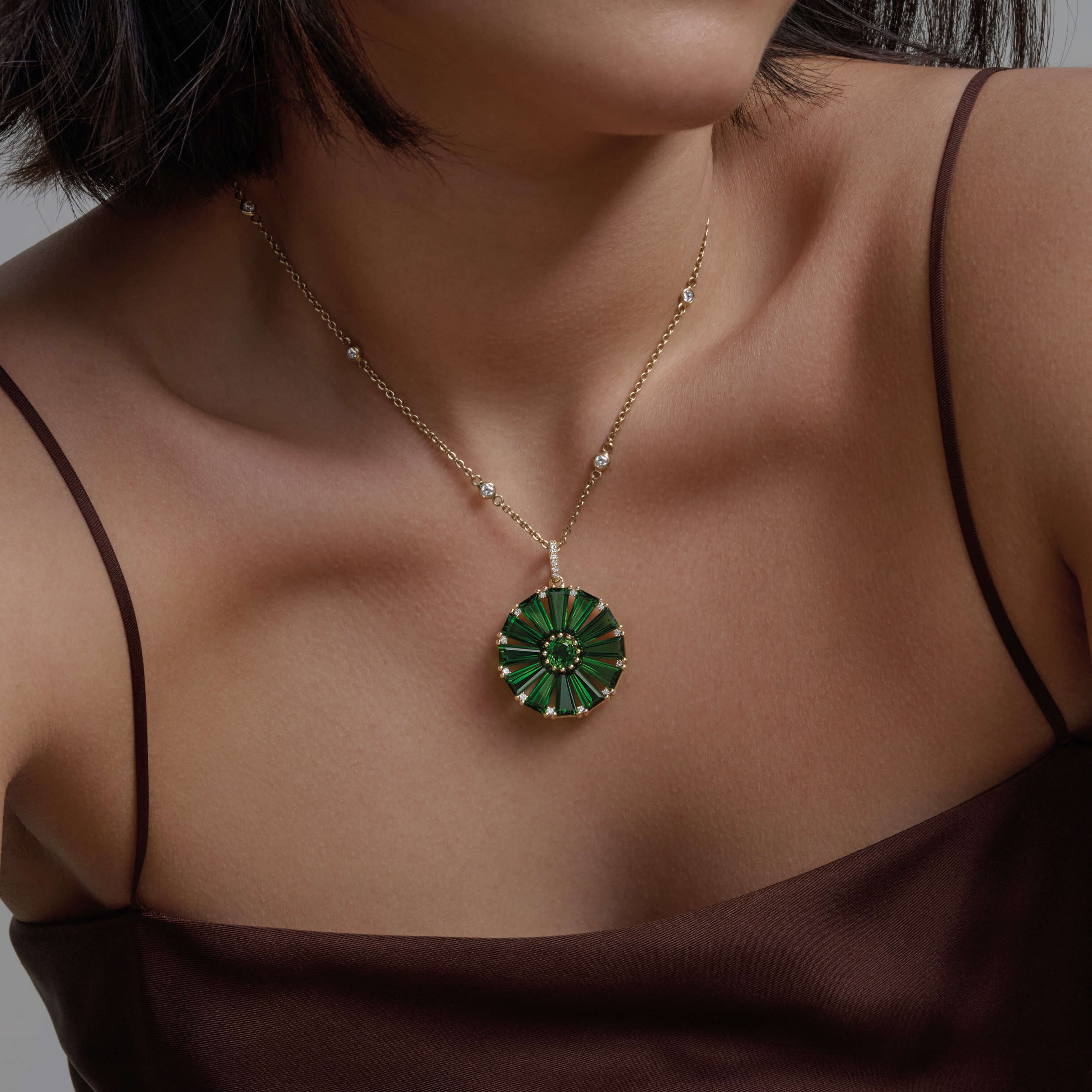 Model wearing a handcrafted yellow gold circular necklace pendant with baguette cut chrome diopside and diamond gemstones.