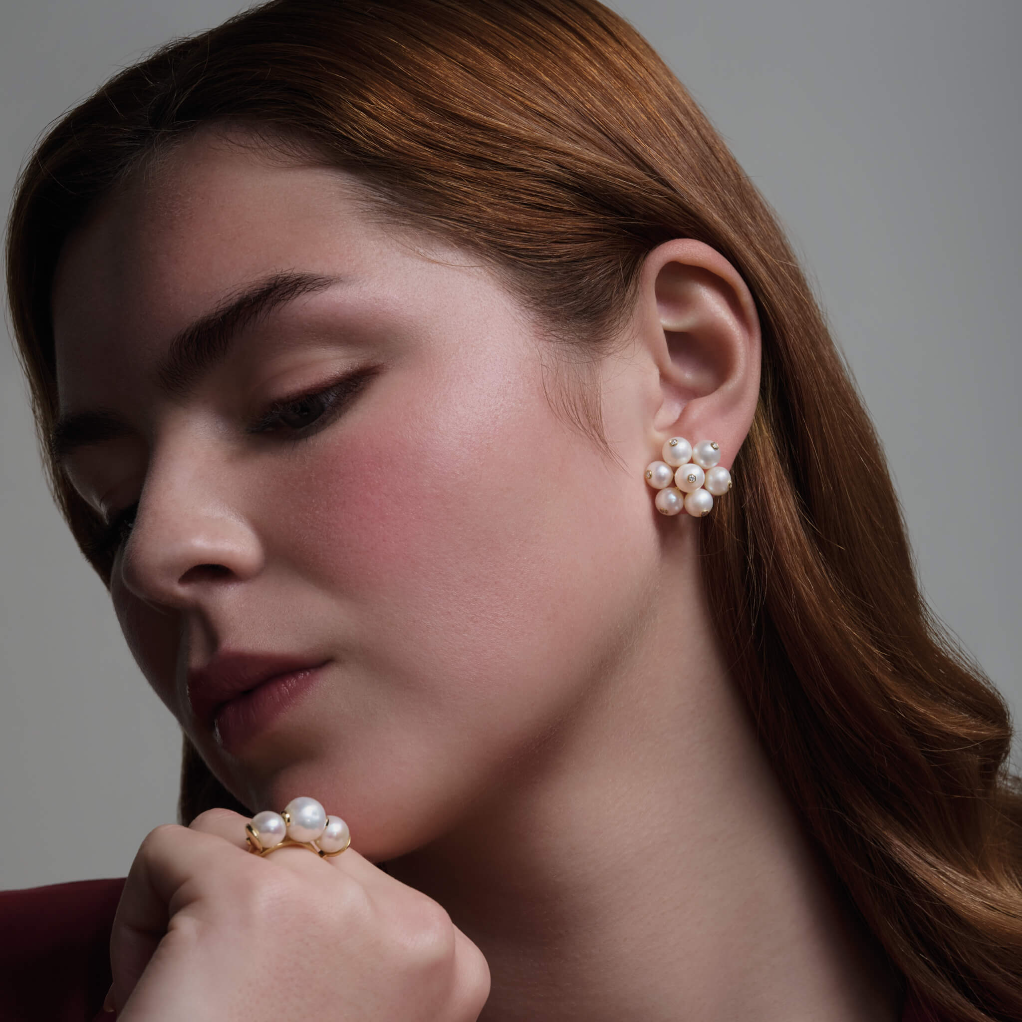 Model wearing handcrafted earrings in 18ct yellow gold featuring a cluster of white pearls. The pearls are interspersed with small diamonds.