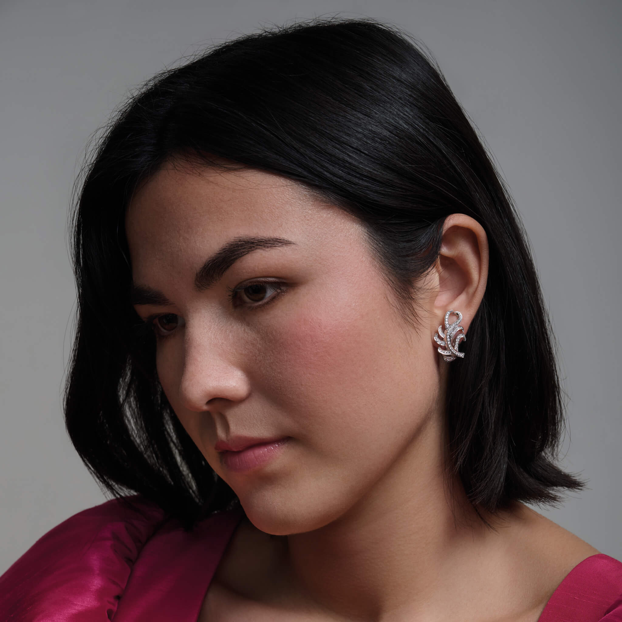 Model wears handcrafted earrings in the shape of a feather plume in 18ct white gold with diamond pavé.