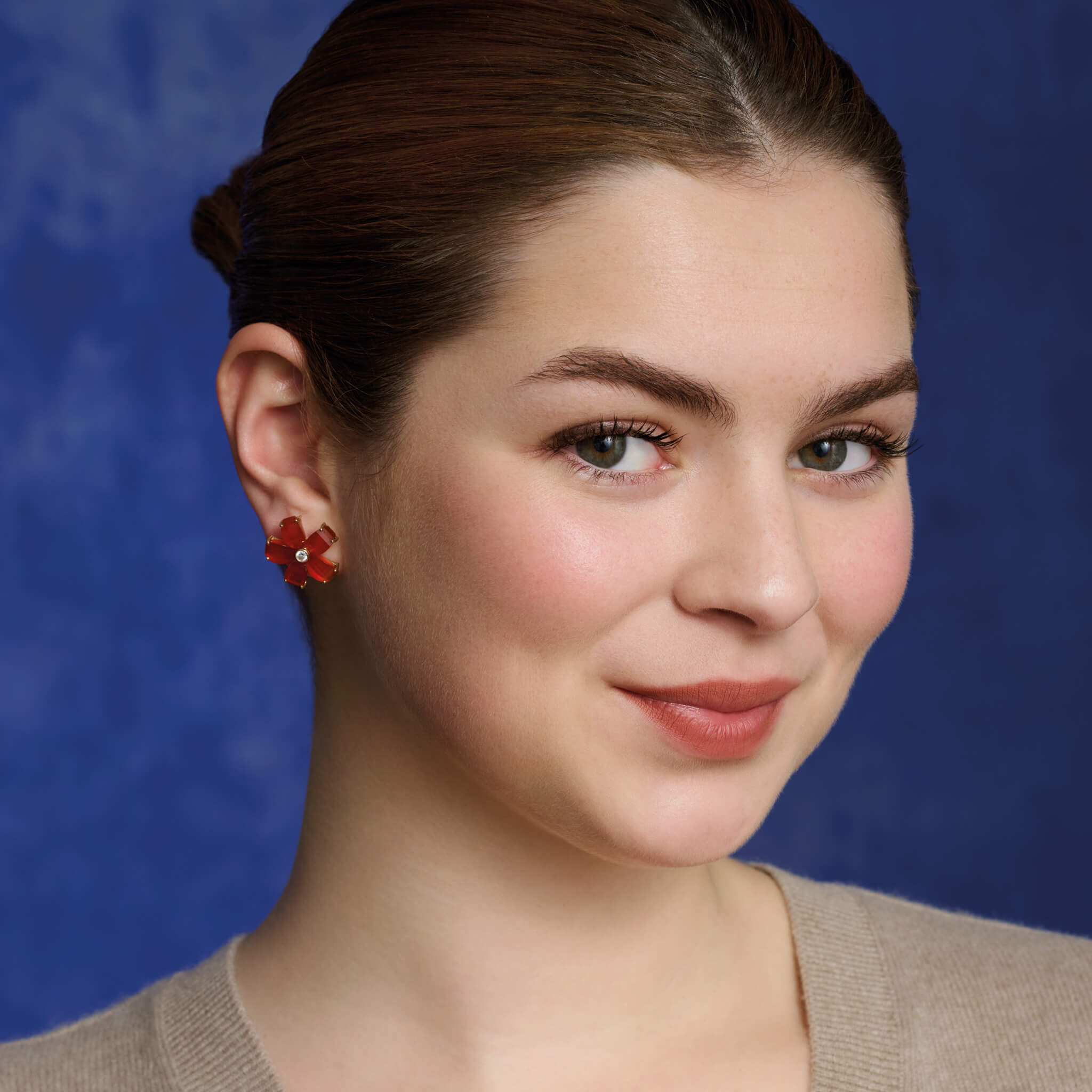 Model wears handcrafted yellow gold flower earring studs featuring five cornelian petals and a central diamond.