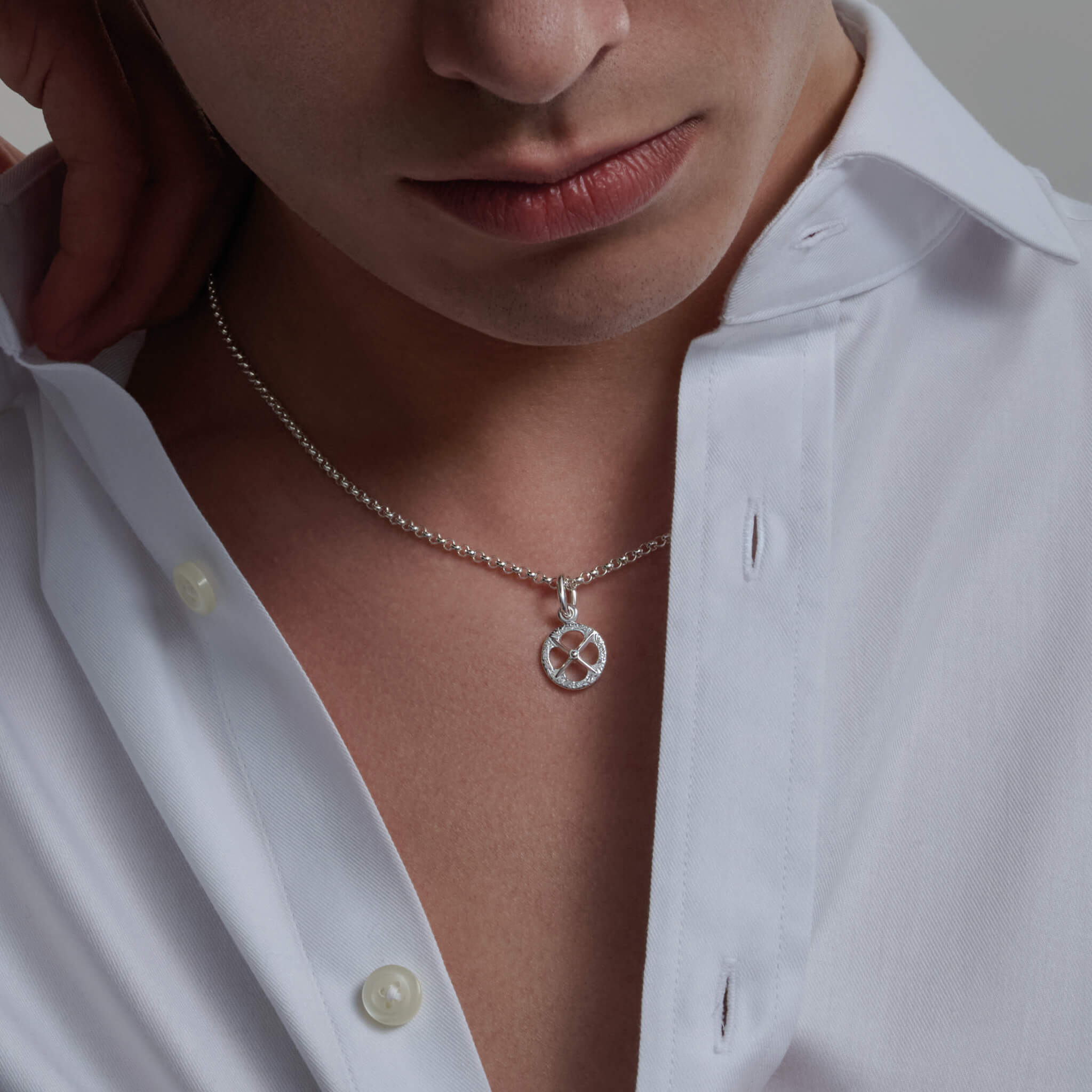 Model wears a handcrafted sterling silver necklace pendant with a circular motif and a cross in the middle.