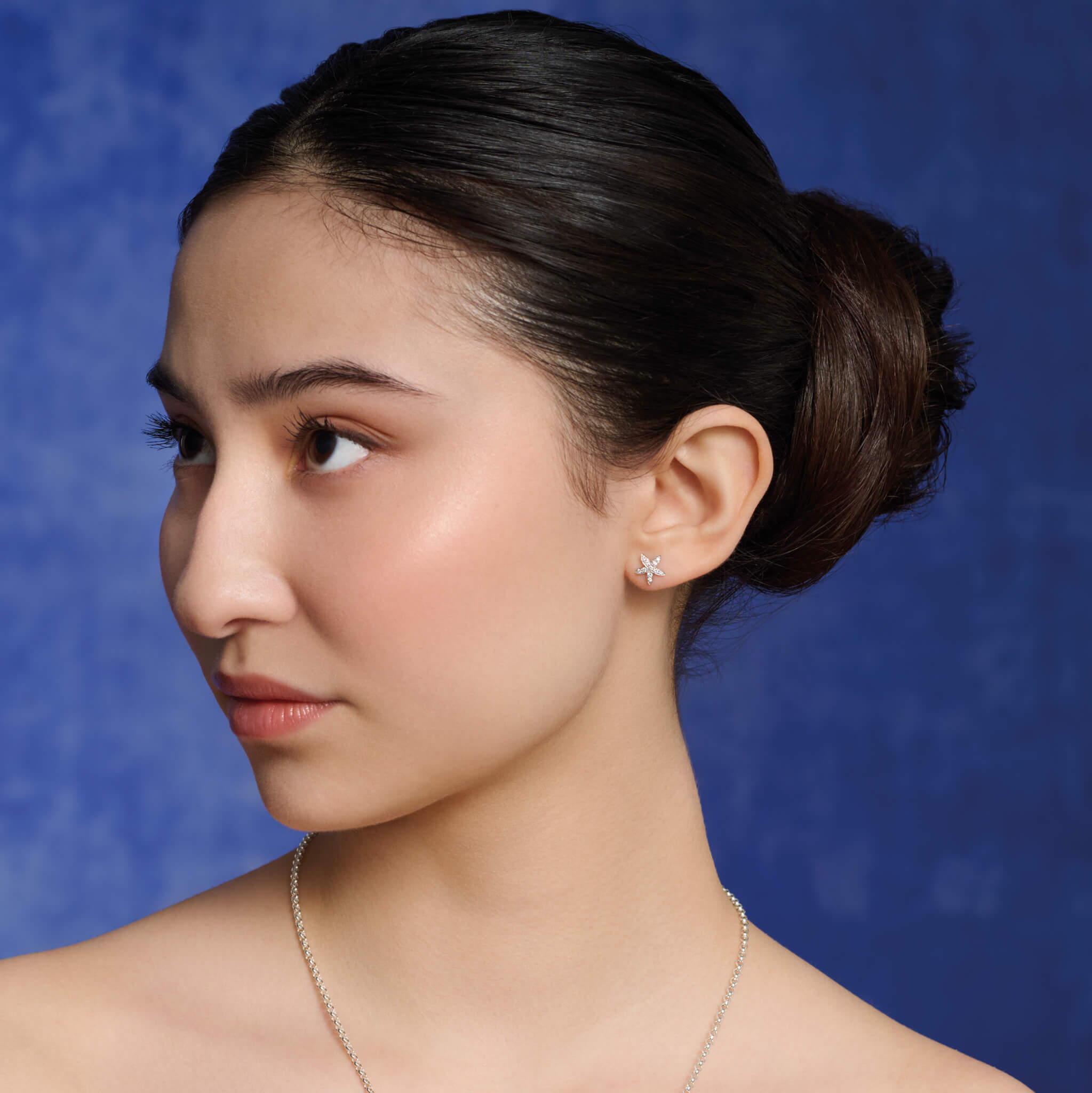 Model wears starfish shaped earrings in precious metal.