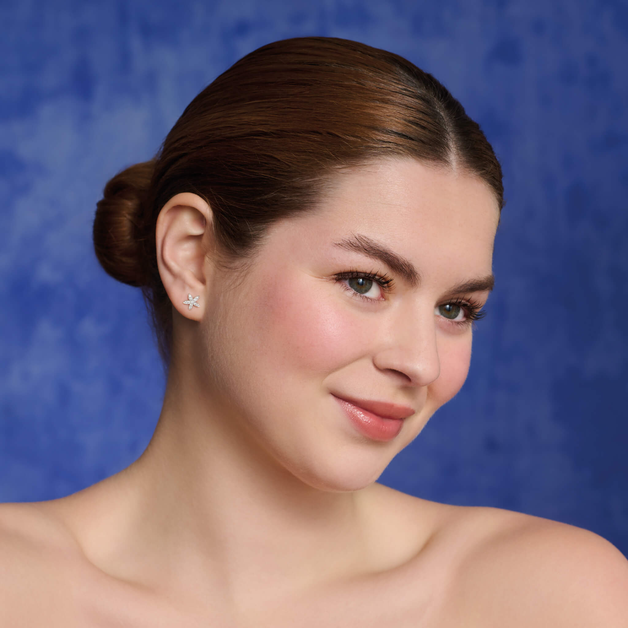 Model wears starfish shaped small stud earrings in precious metal.