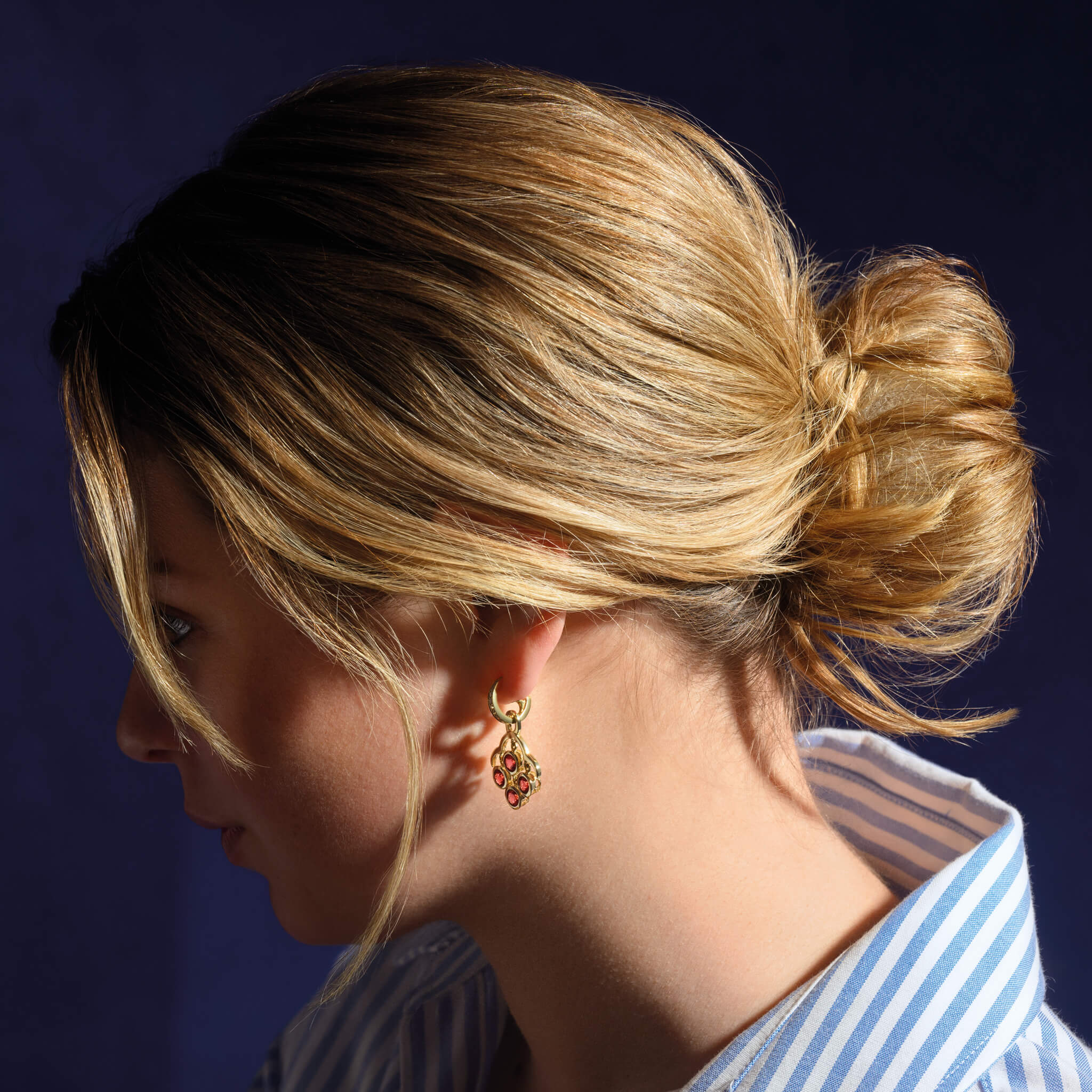 Model wears handcrafted yellow gold earring drops inspired by acai berries featuring four facetted garnet gemstones, on Astrea hoops.