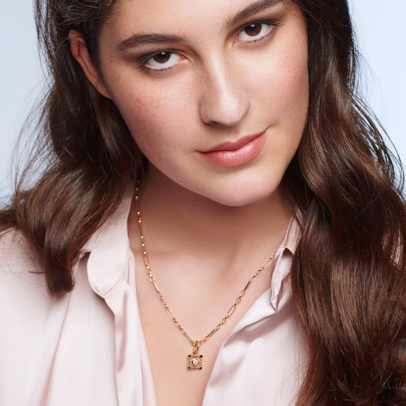 Model wearing a handcrafted necklace pendant featuring a square-shaped frame in precious metal with a central precious stone.