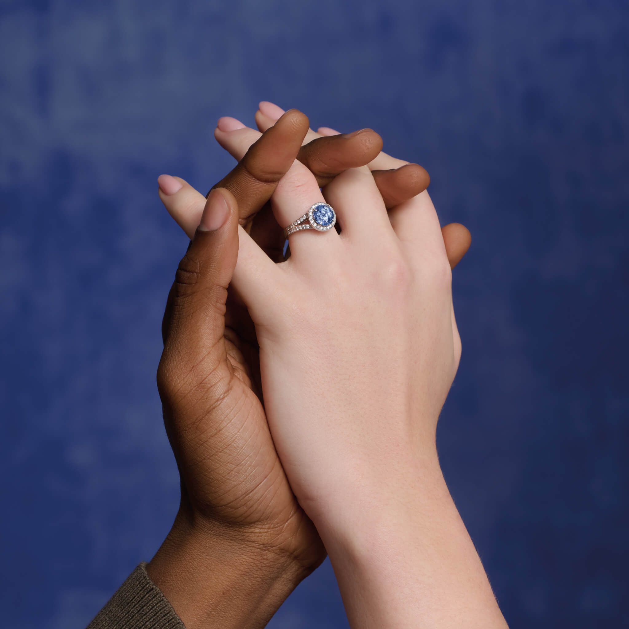 Model wears handcrafted 18ct white gold engagement ring with a large round central sapphire surrounded by a halo of small diamonds and smaller diamonds embedded along the band.