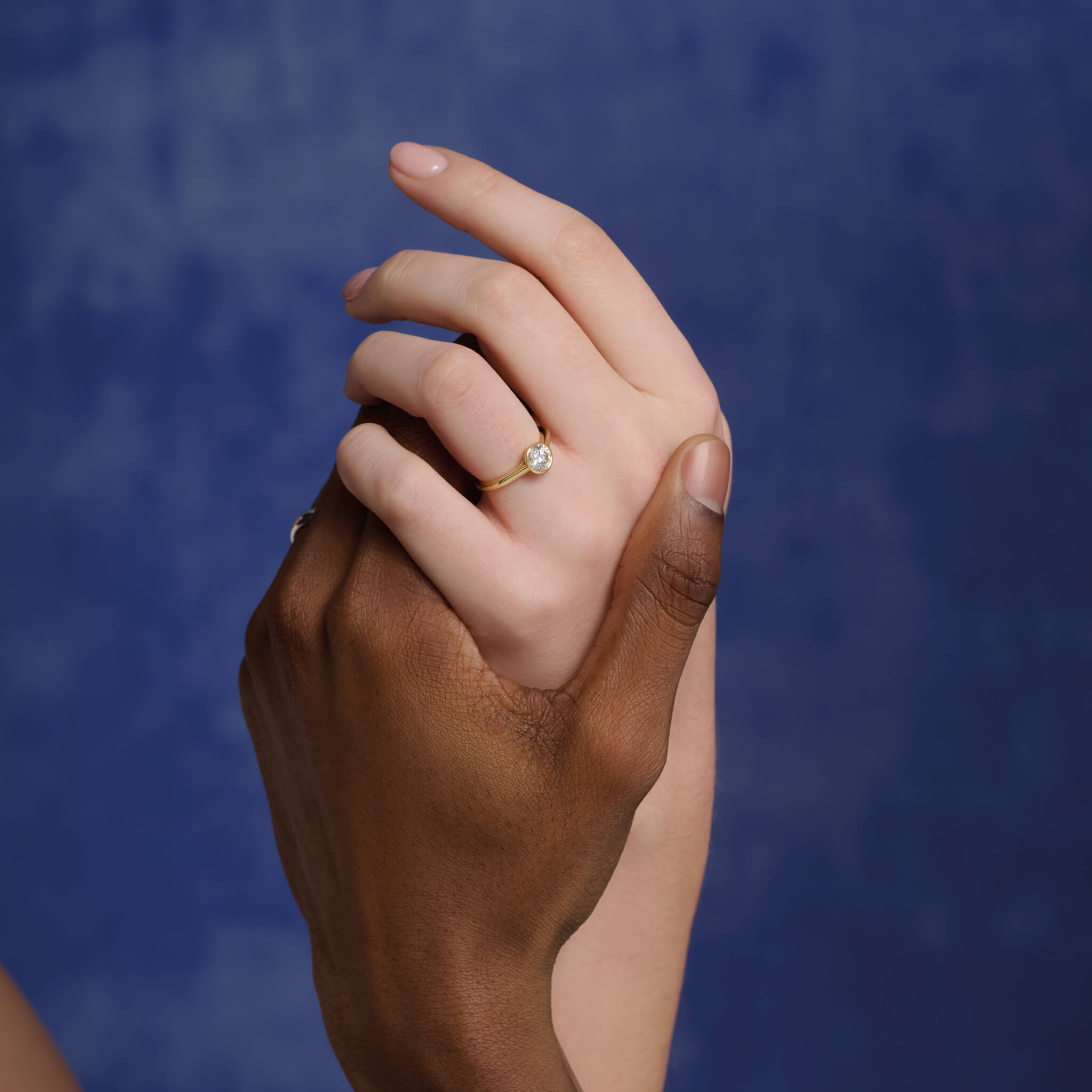 Model wears handmade 18ct yellow gold engagement ring featuring a round central diamond in a rub over setting.