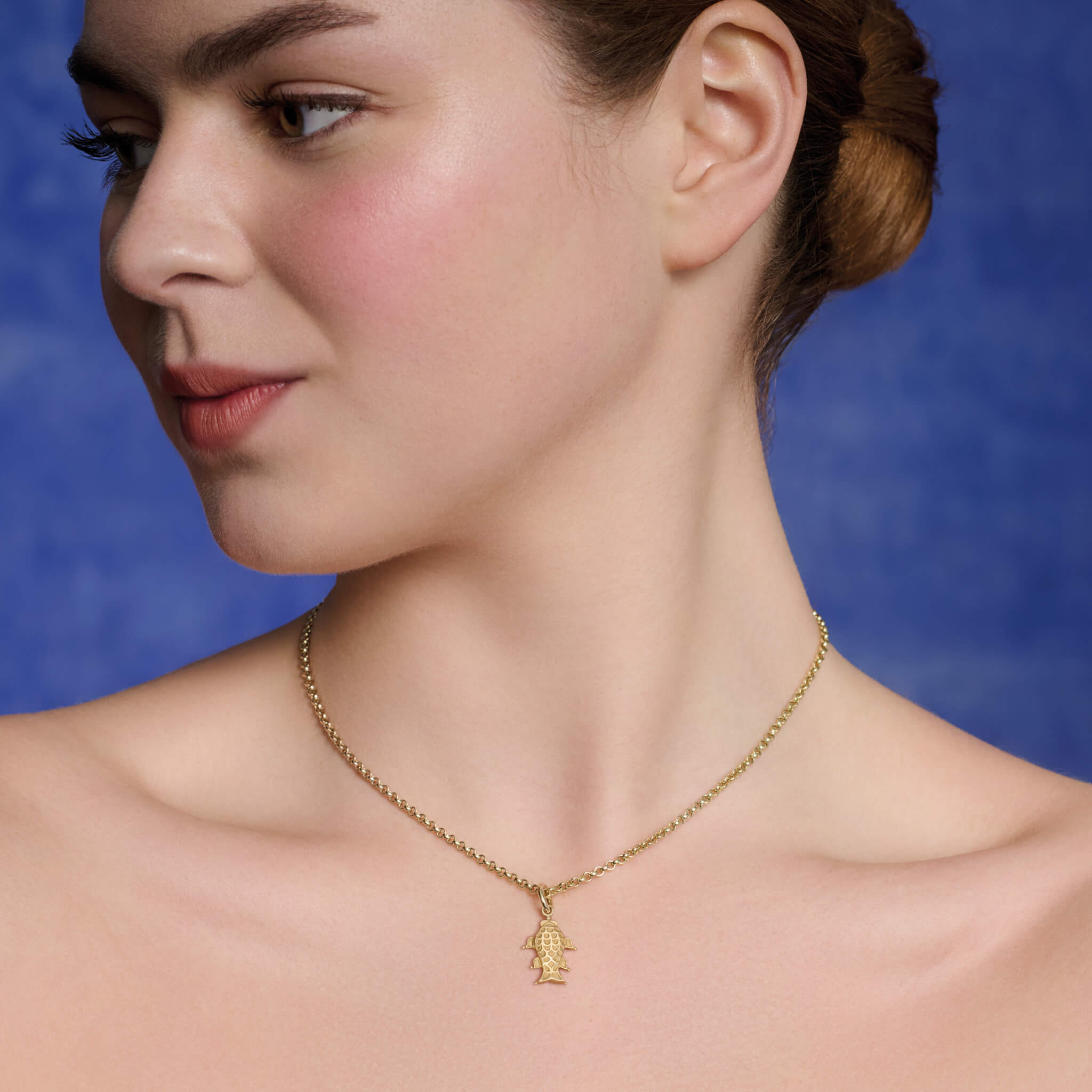 Model wears handcrafted yellow gold fish shaped necklace pendant.