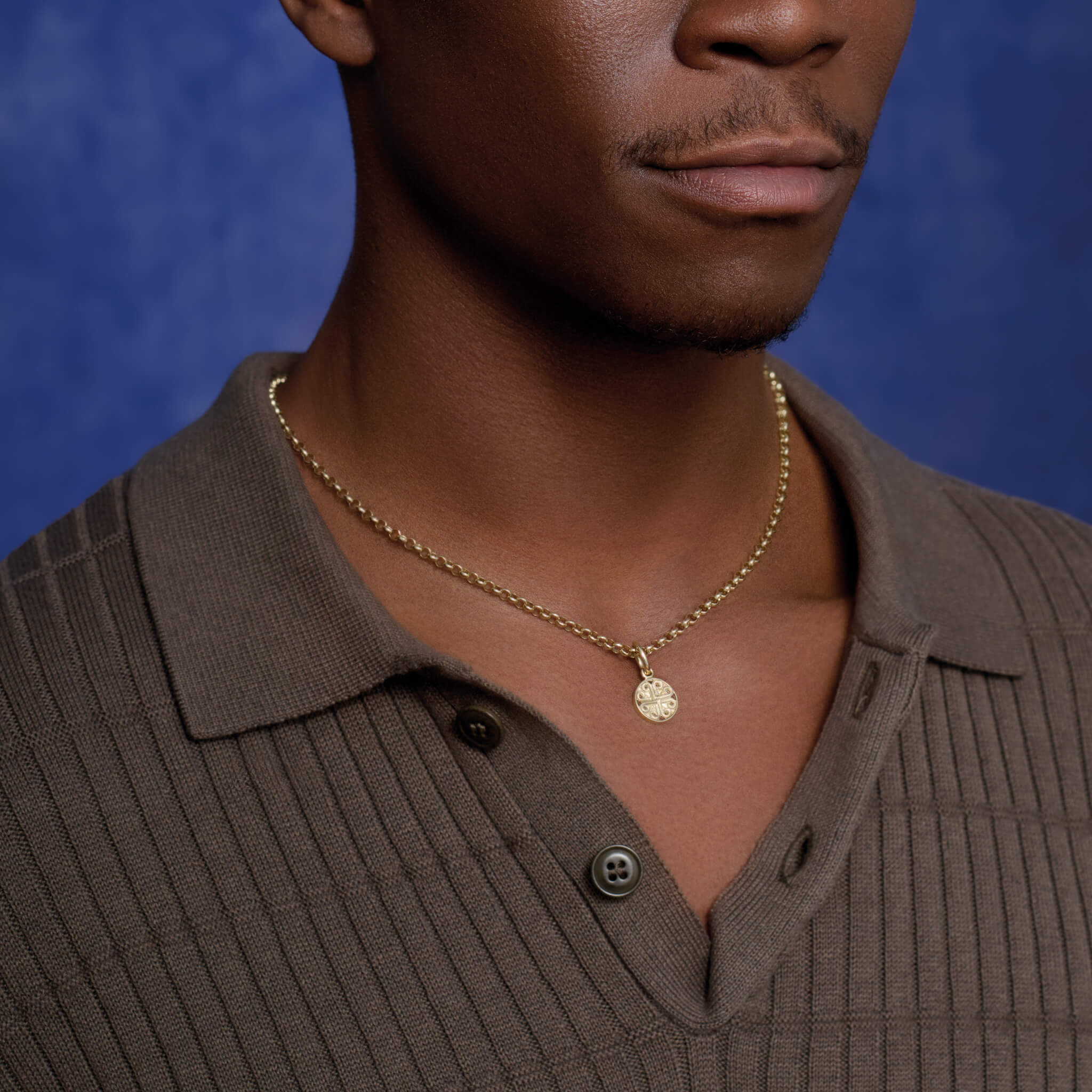 Model wears the handcrafted Kefalonia necklace pendant in 9ct yellow gold. A circular shaped necklace pendant with a cross-like motif in the centre.