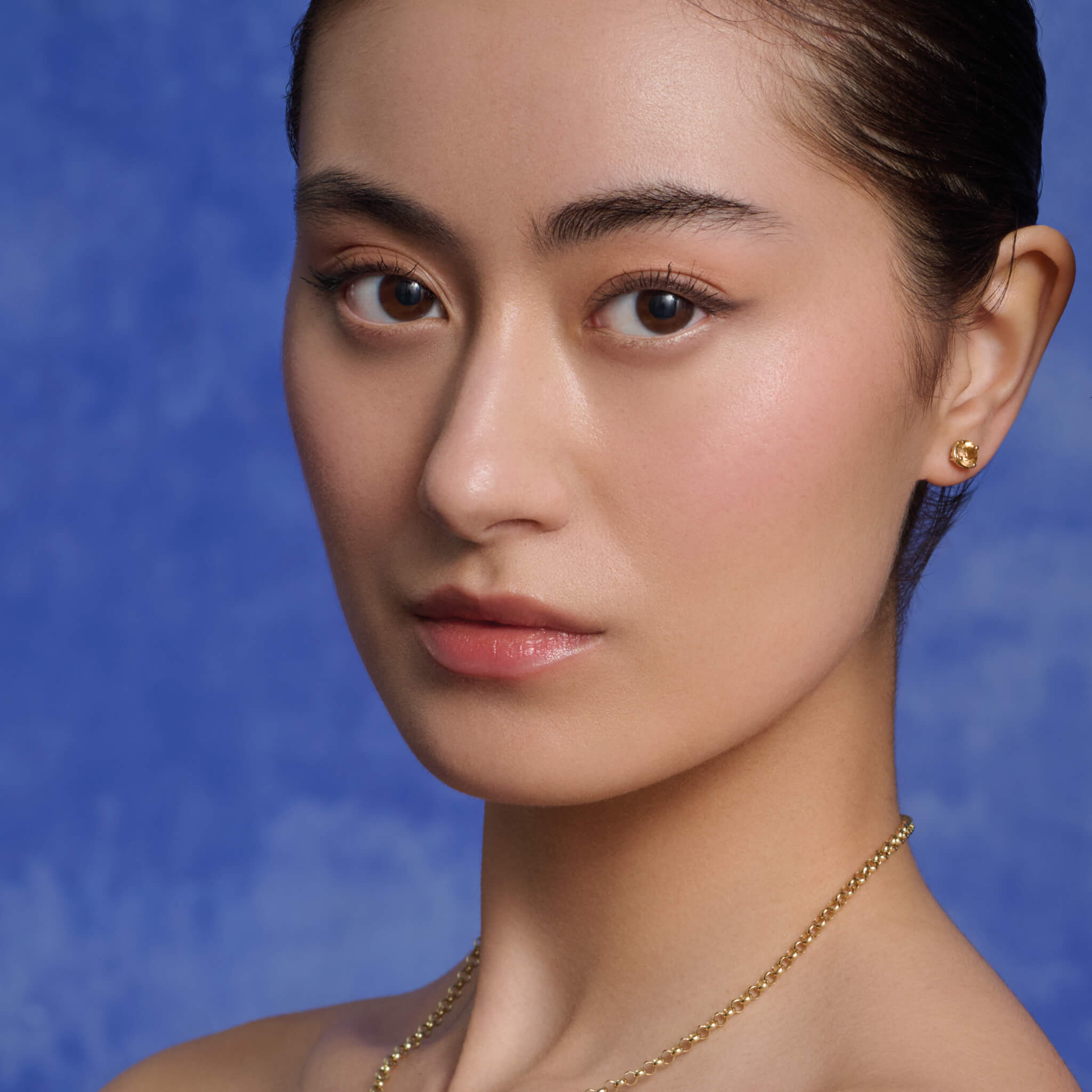 Model wears handcrafted 18ct yellow gold interchangeable stud earrings featuring precious gemstone.