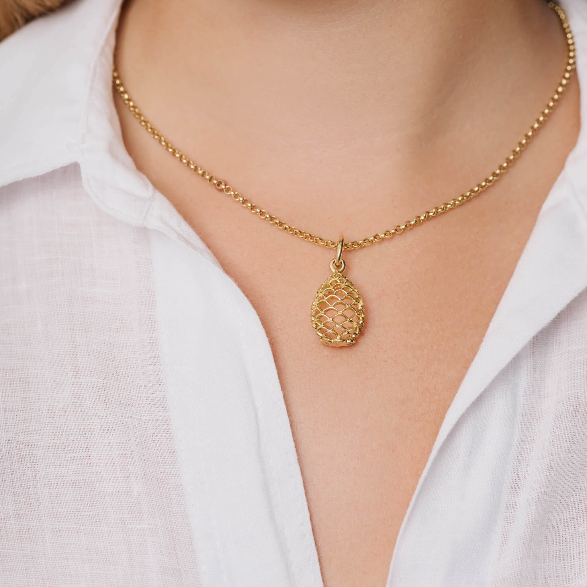 Model wearing a handcrafted yellow gold necklace pendant featuring a pinecone frame.