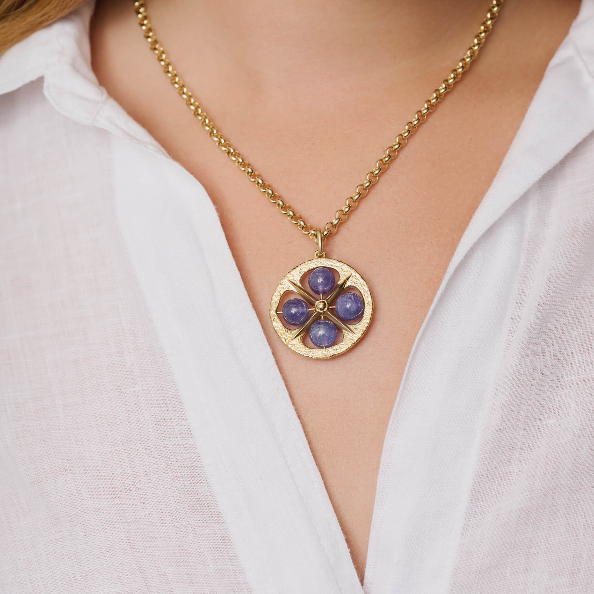 Model wears handcrafted 9ct yellow gold necklace pendant with a circular motif and a cross in the middle and four tanzanite beads.