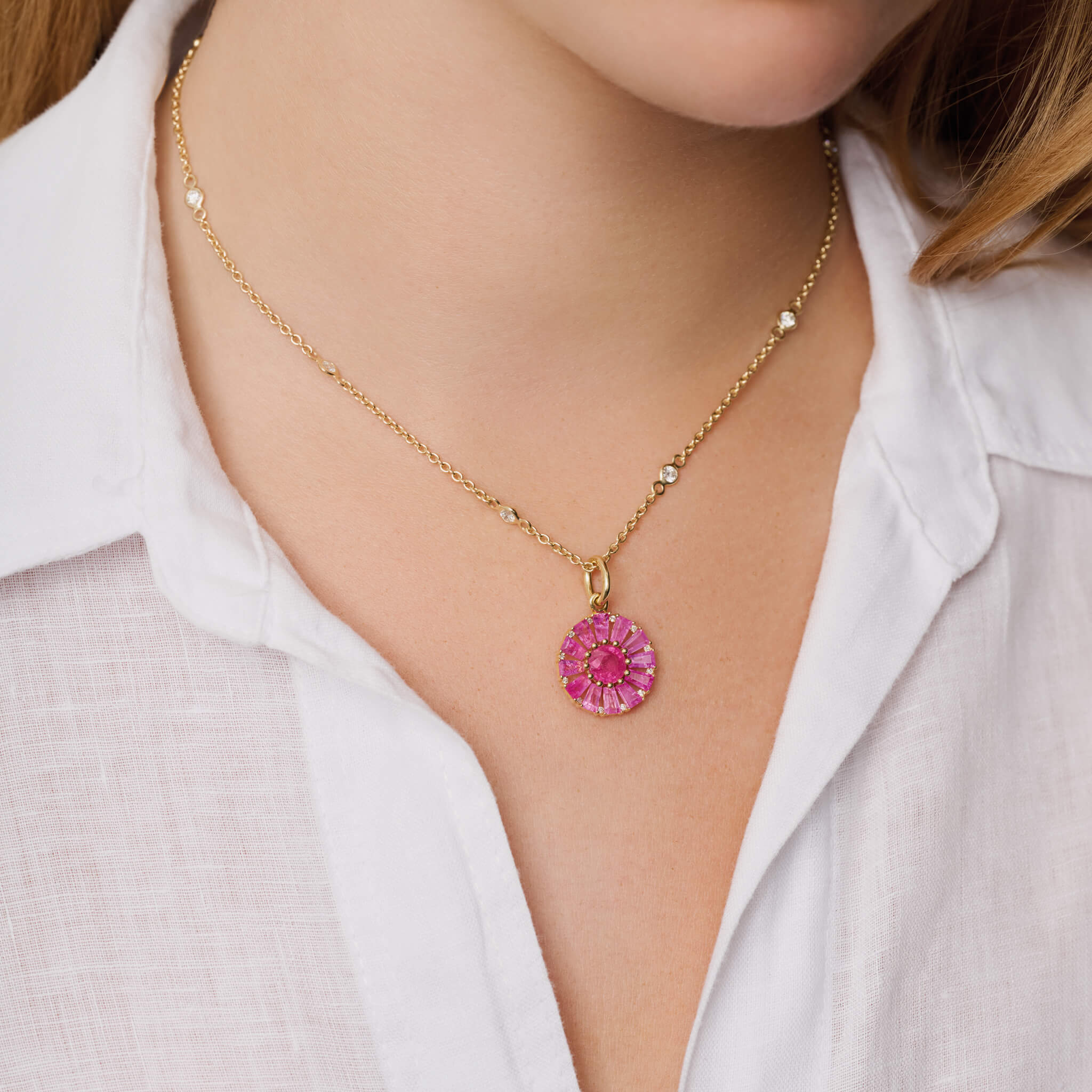 Model wears handcrafted 18ct yellow gold necklace pendant featuring a circular arrangement of pink sapphire and a central pink sapphire interspaced with diamonds.