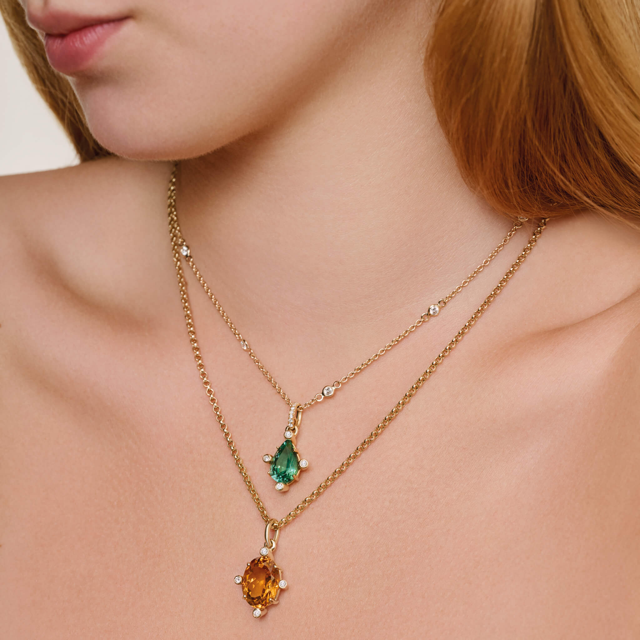 Model wearing handcrafted 18ct yellow gold pendant with pear facetted green gemstone set with four diamonds. on gold chain with diamonds.