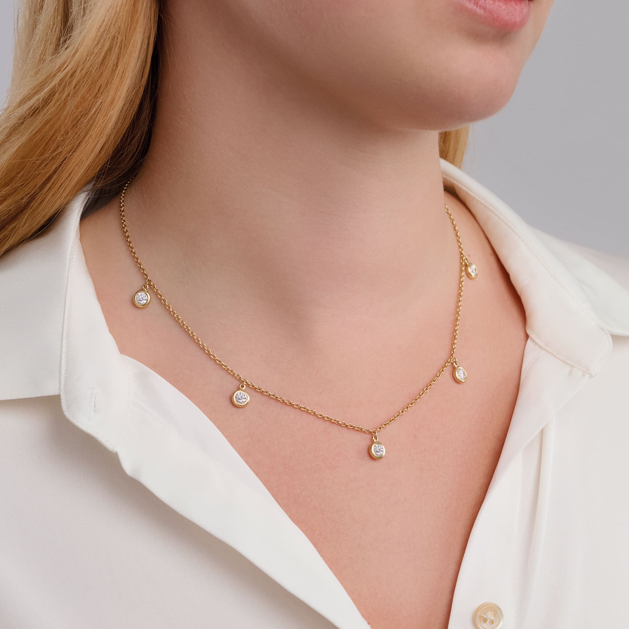 Model wearing a handcrafted necklace in precious metal with five round precious stone drops.