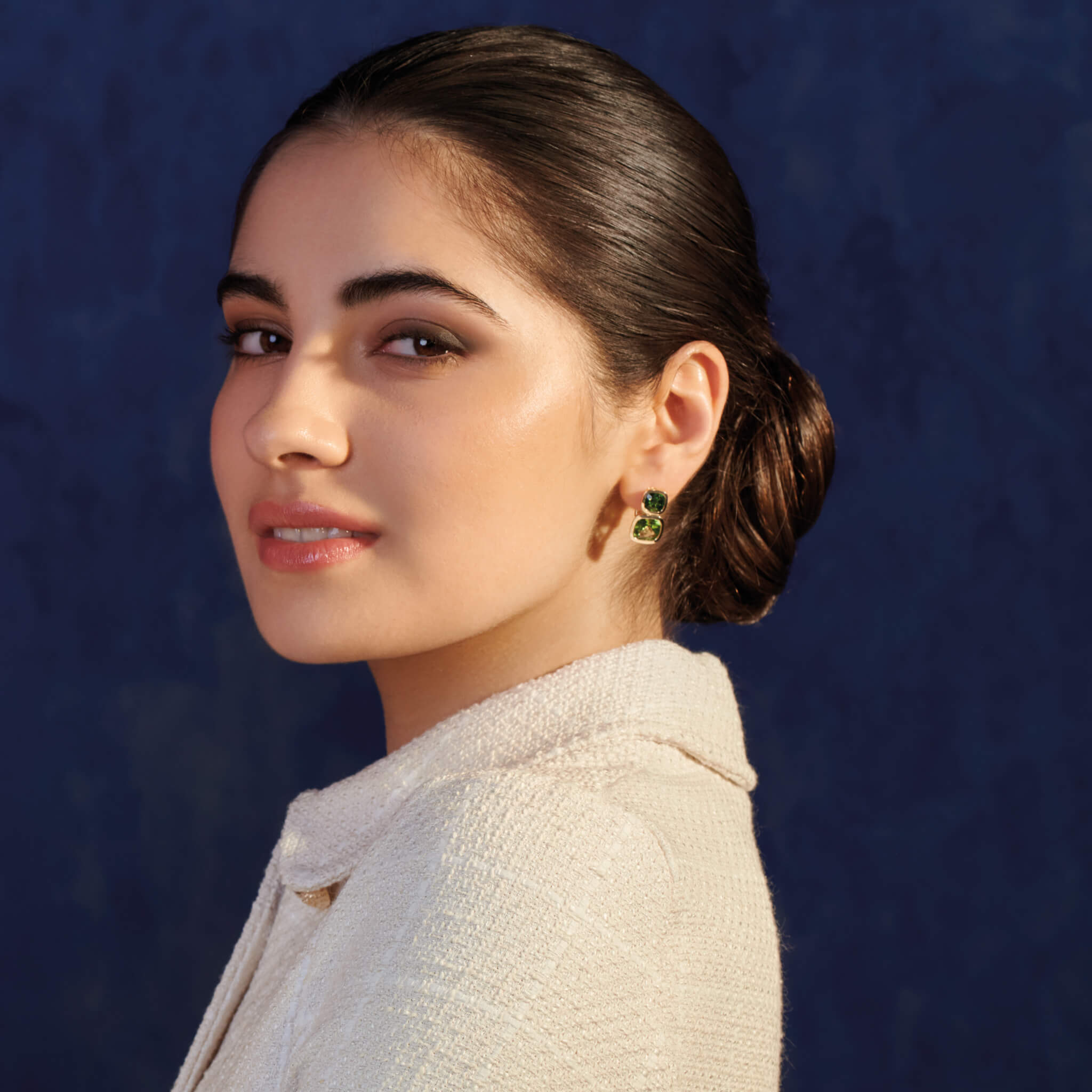 Model wears handcrafted 18ct yellow gold square shaped earrings featuring chrome diopside and peridot gemstones.