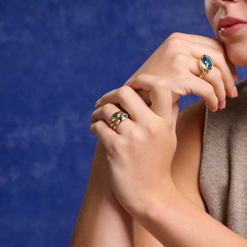 Model wearing a handcrafted yellow gold ring with a slight teardrop design set with oval facetted gemstones.