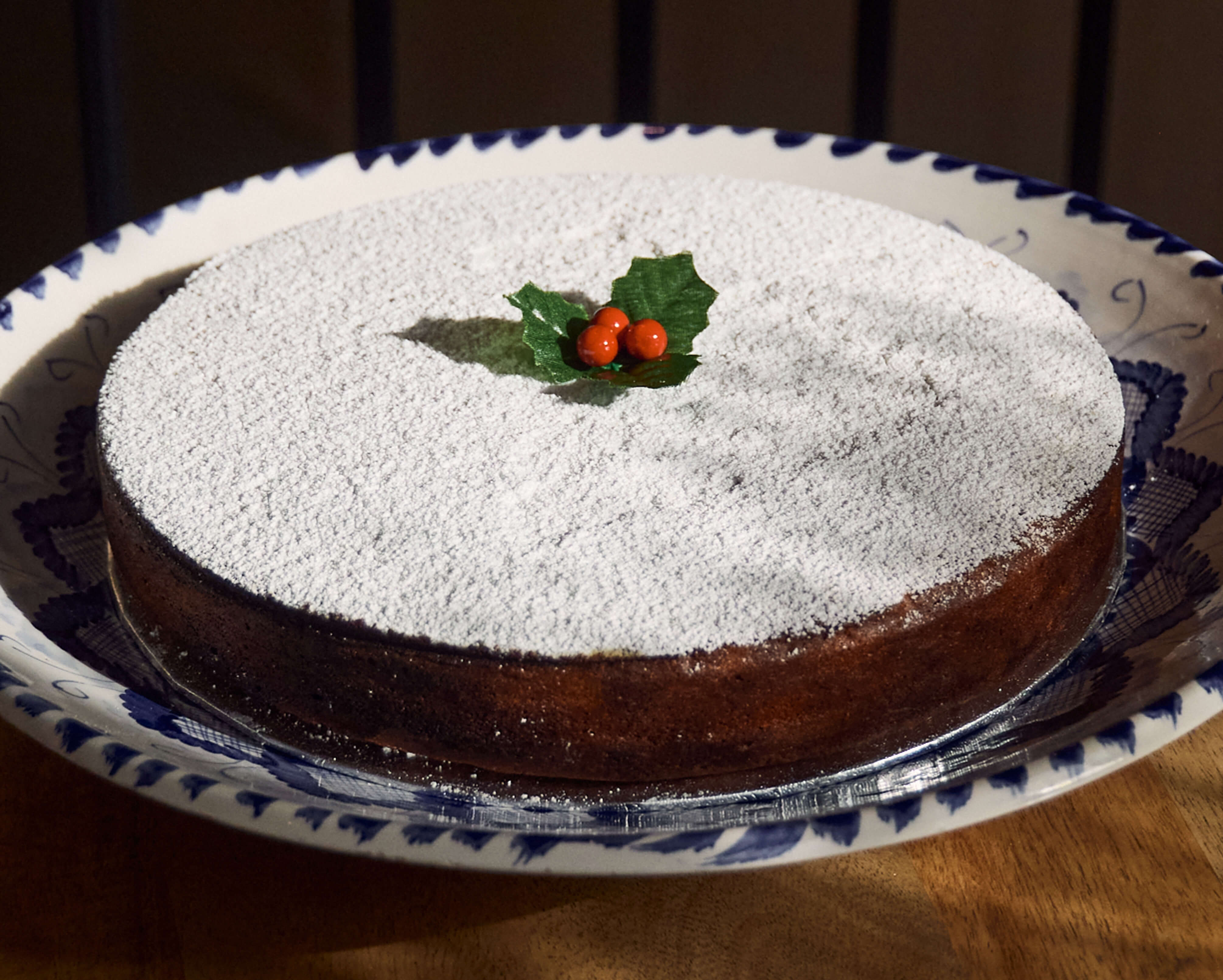 Greek epiphany chocolate cake with powdered sugar and holly decoration on a decorative plate to celebrate the Vasilopita tradition.