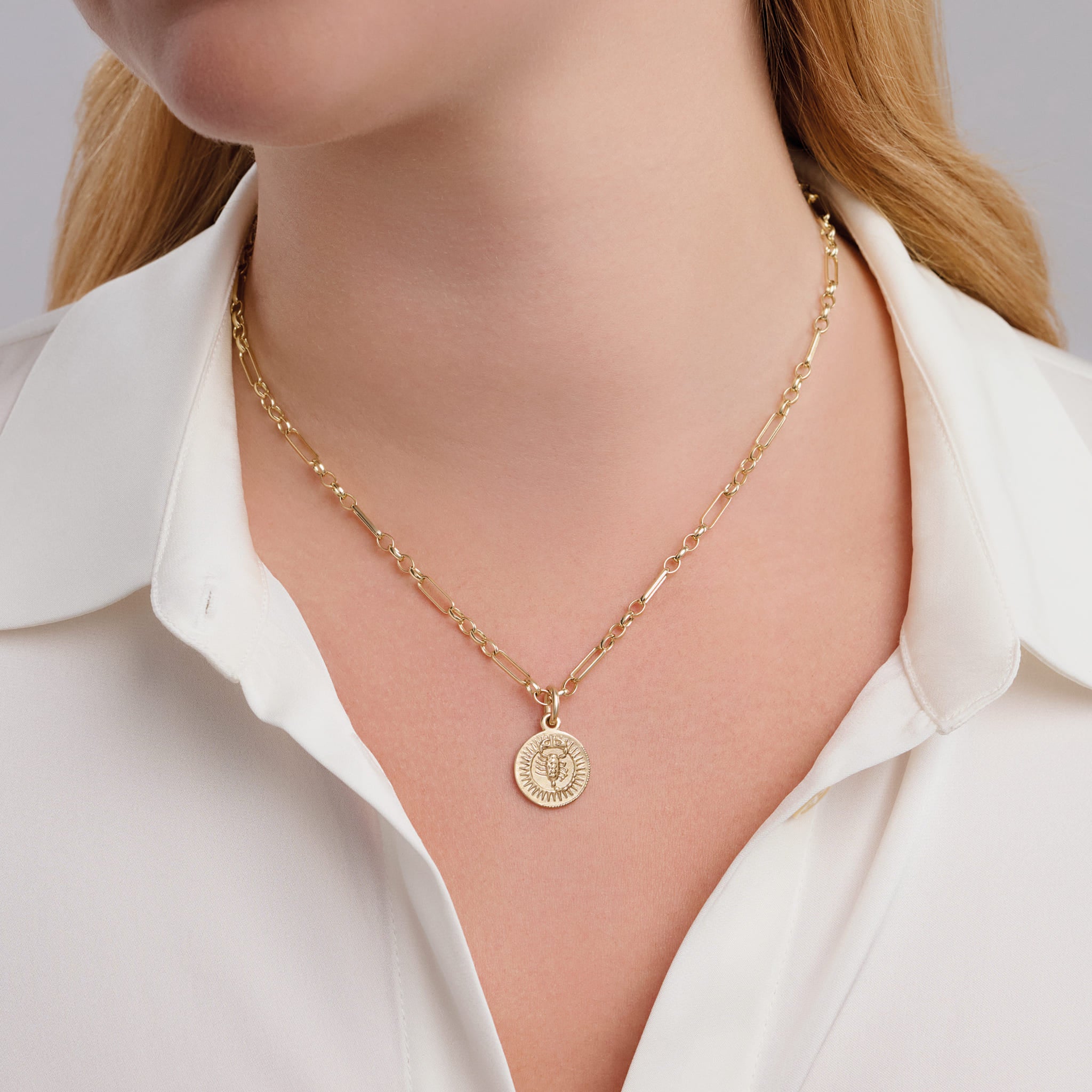 Model wearing handcrafted round yellow gold necklace pendant engraved with the zodiac scorpio.