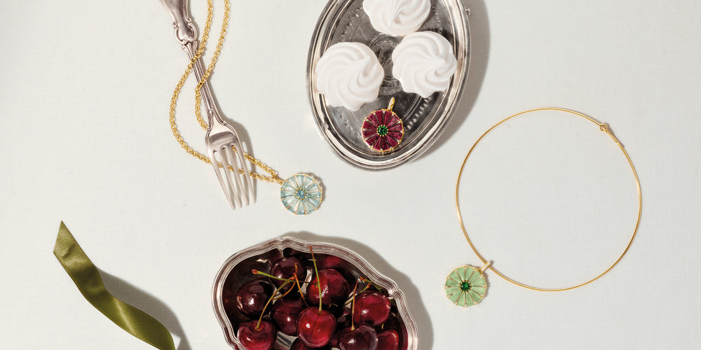 Roi Soleil pendants in yellow gold with different colourful gemstones on a background with silver trays and cutlery