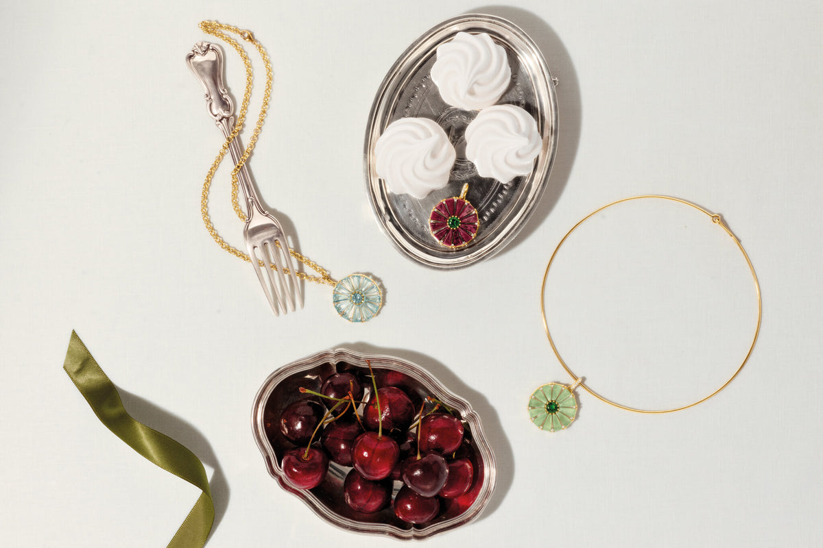 Roi Soleil pendants in yellow gold with different colourful gemstones on a background with silver trays and cutlery