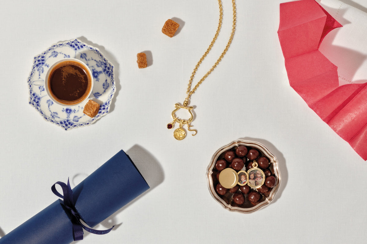 Chatelaine charm holder and Annie locket on white table cloth with Christmas cracker,  paper crown, coffee and sugar cubes.