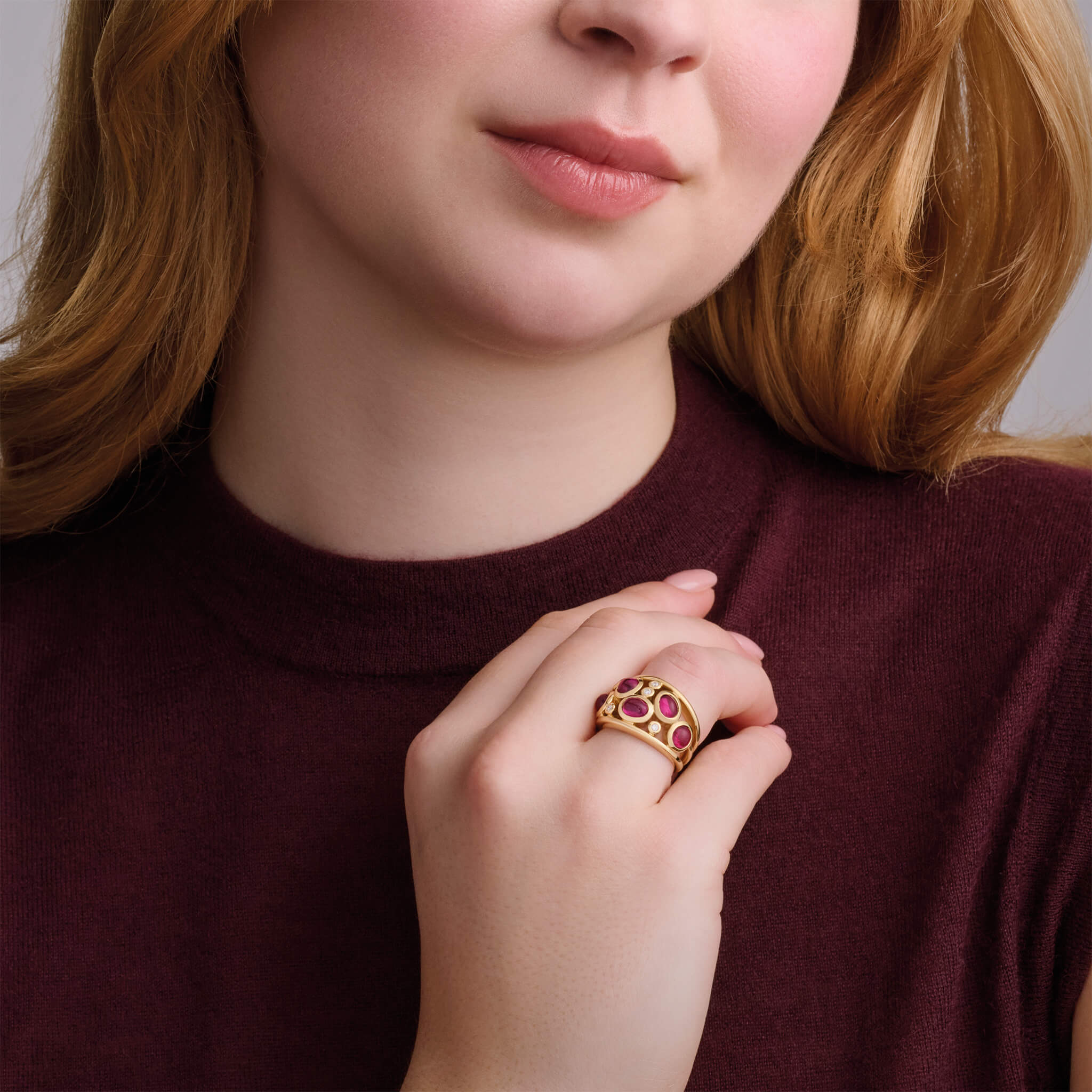 Model wearing  handcrafted 18ct yellow gold ring featuring four precious gemstones and smaller diamonds.