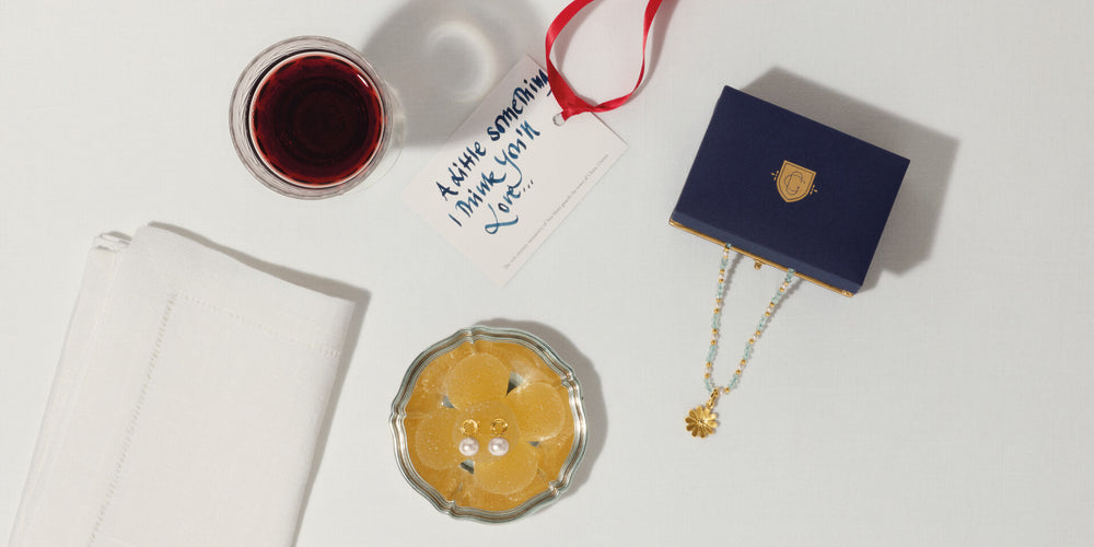Alpha & Omega stud earrings and Anemone necklace pendant on table with handwritten card, wine, and napkin.
