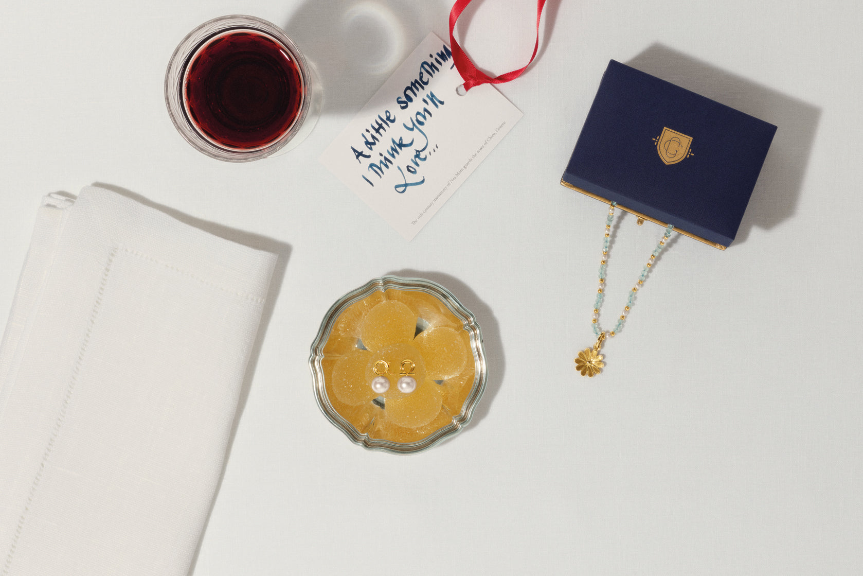 Alpha & Omega stud earrings and Anemone necklace pendant on table with handwritten card, wine, and napkin.