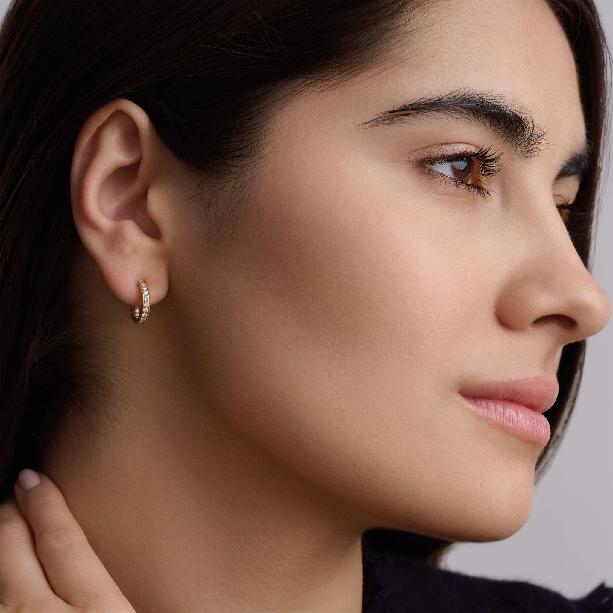 Model wearing a handcrafted 18ct yellow gold hoop earring set with small diamonds.