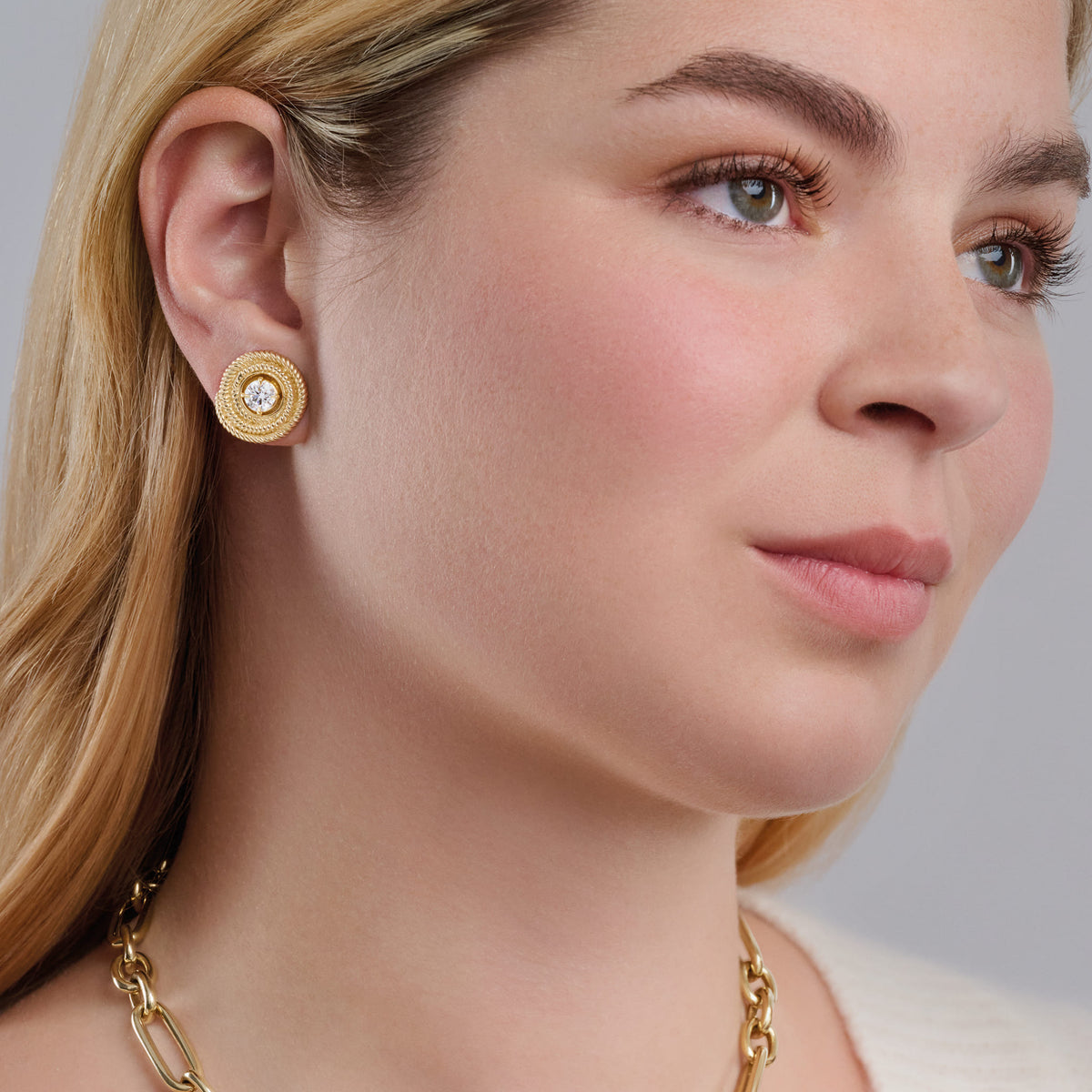 Model wearing handcrafted yellow gold earring halos with a woven swirl design, featuring a round central setting for a stud earring.