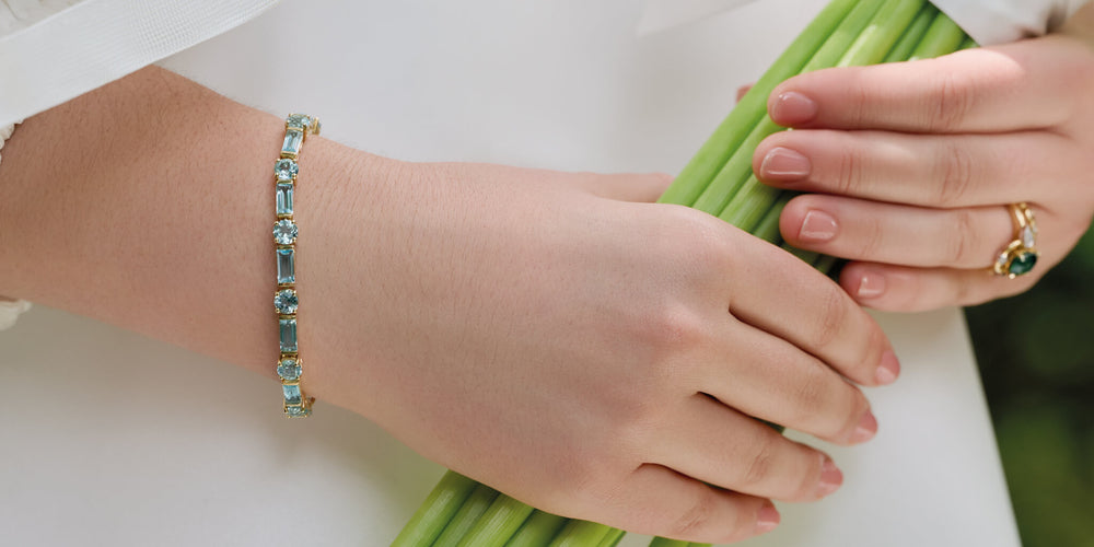 Hands holding a bouquet of flowers wearing Cassandra Goad bridal jewellery such as Roi Soleil bracelet and Compass ring