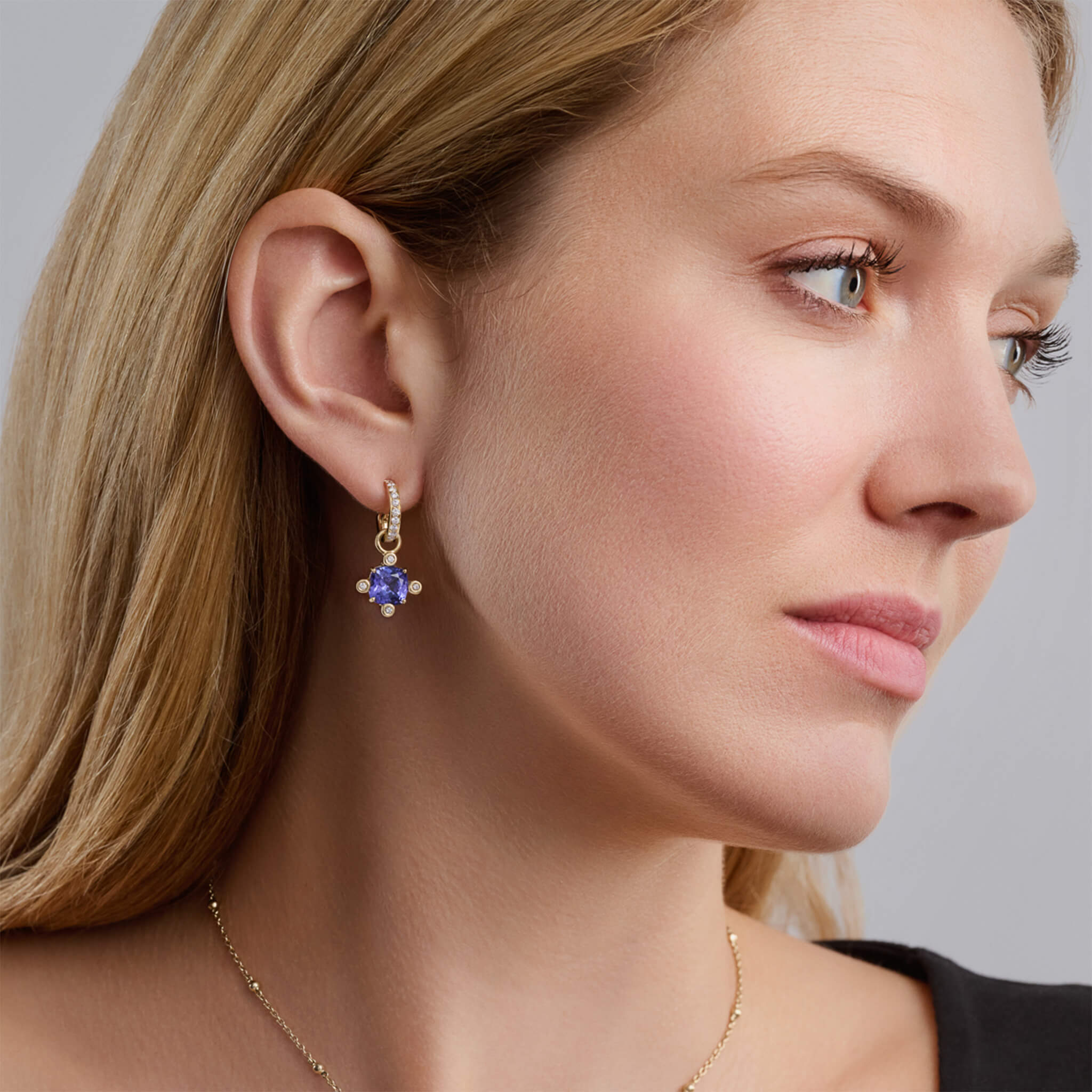 Model wearing handcrafted yellow gold earring drops set with tanzanite cushions and diamonds