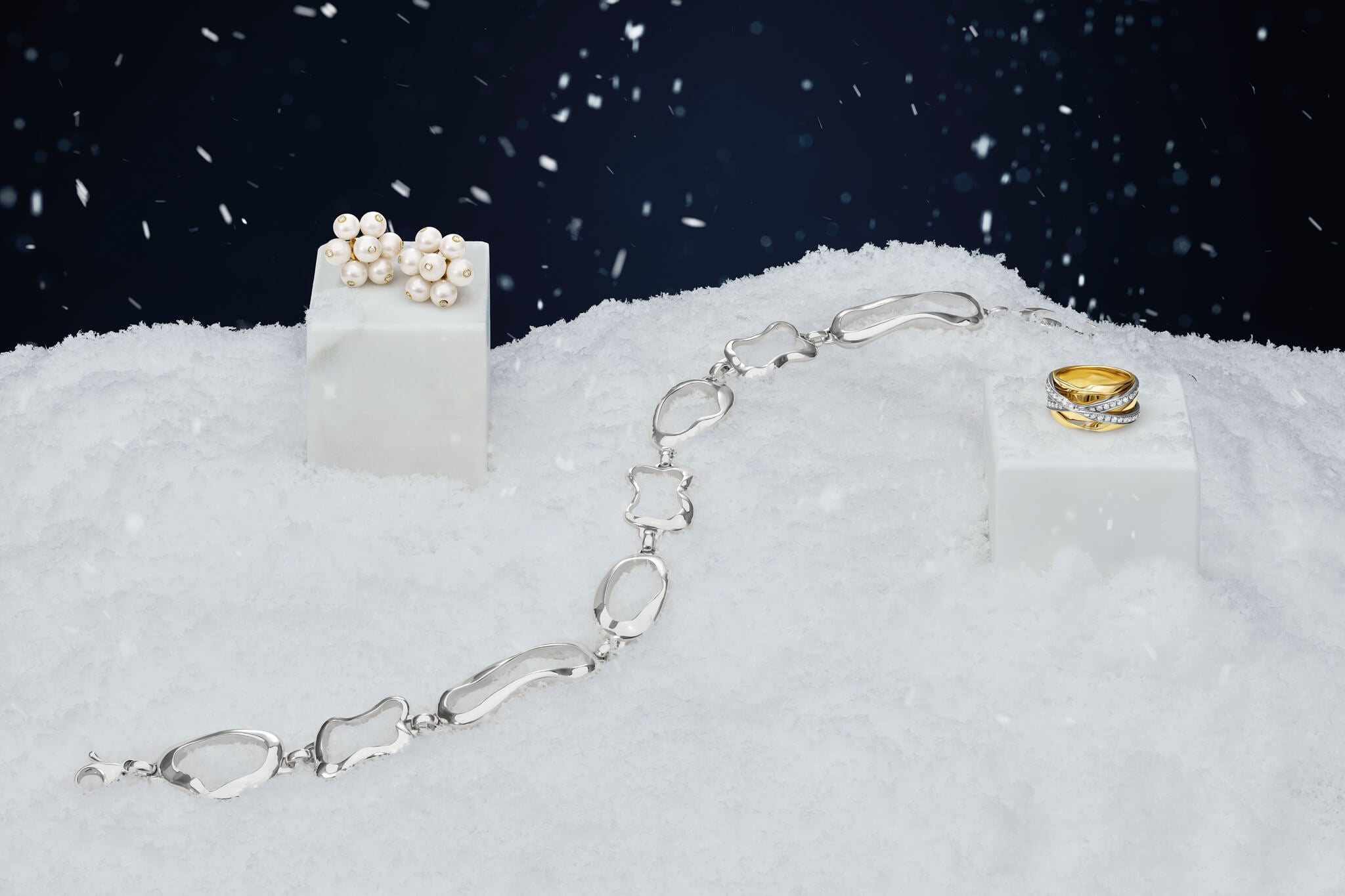 Culinary inspired jewellery for Christmas presents lying on a snowy background. Pearl cluster earrings, silver necklace and yellow gold and while gold diamond ring.