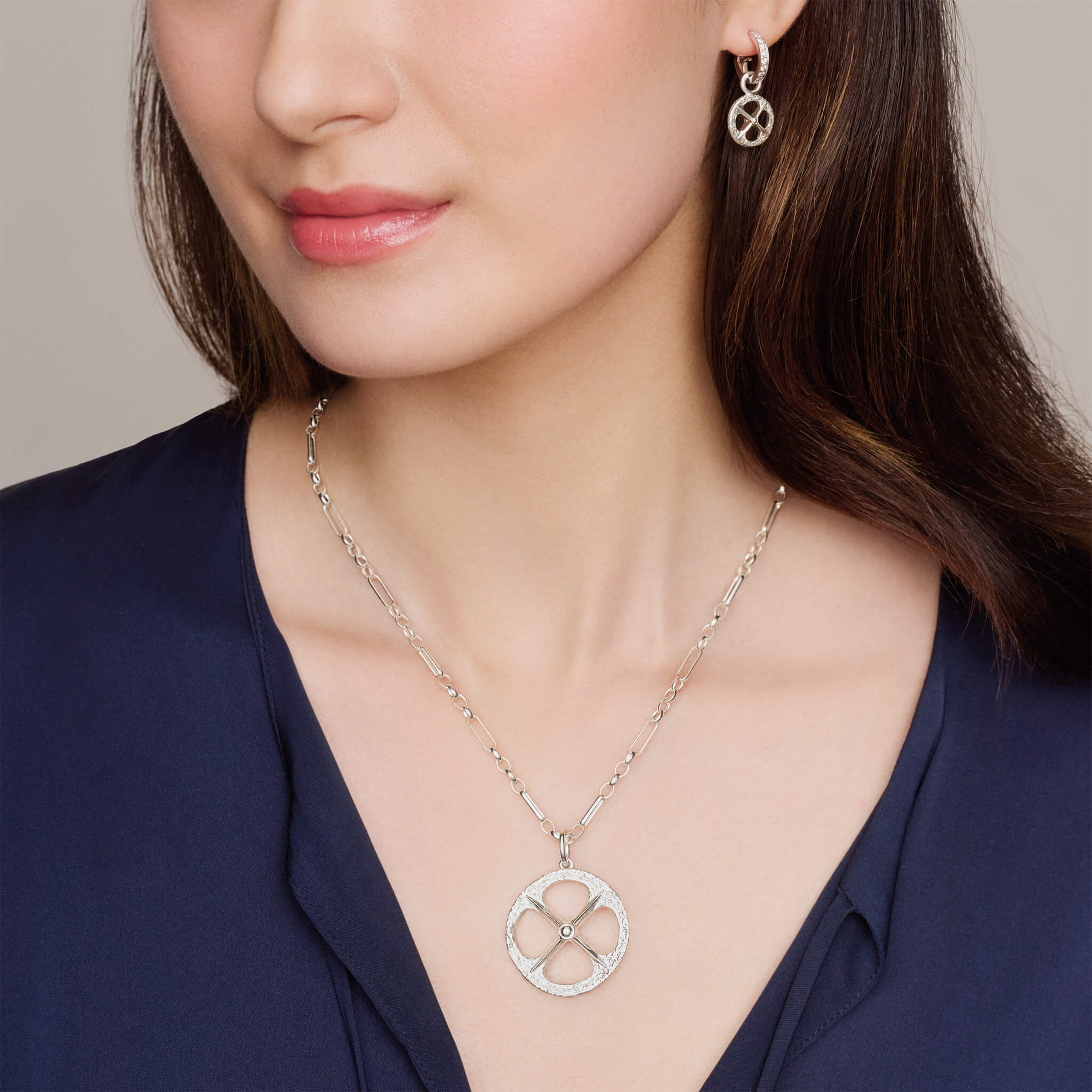 Model wearing handcrafted silver necklace pendant and earring drop with a circular motif and a cross in the middle, helios collection